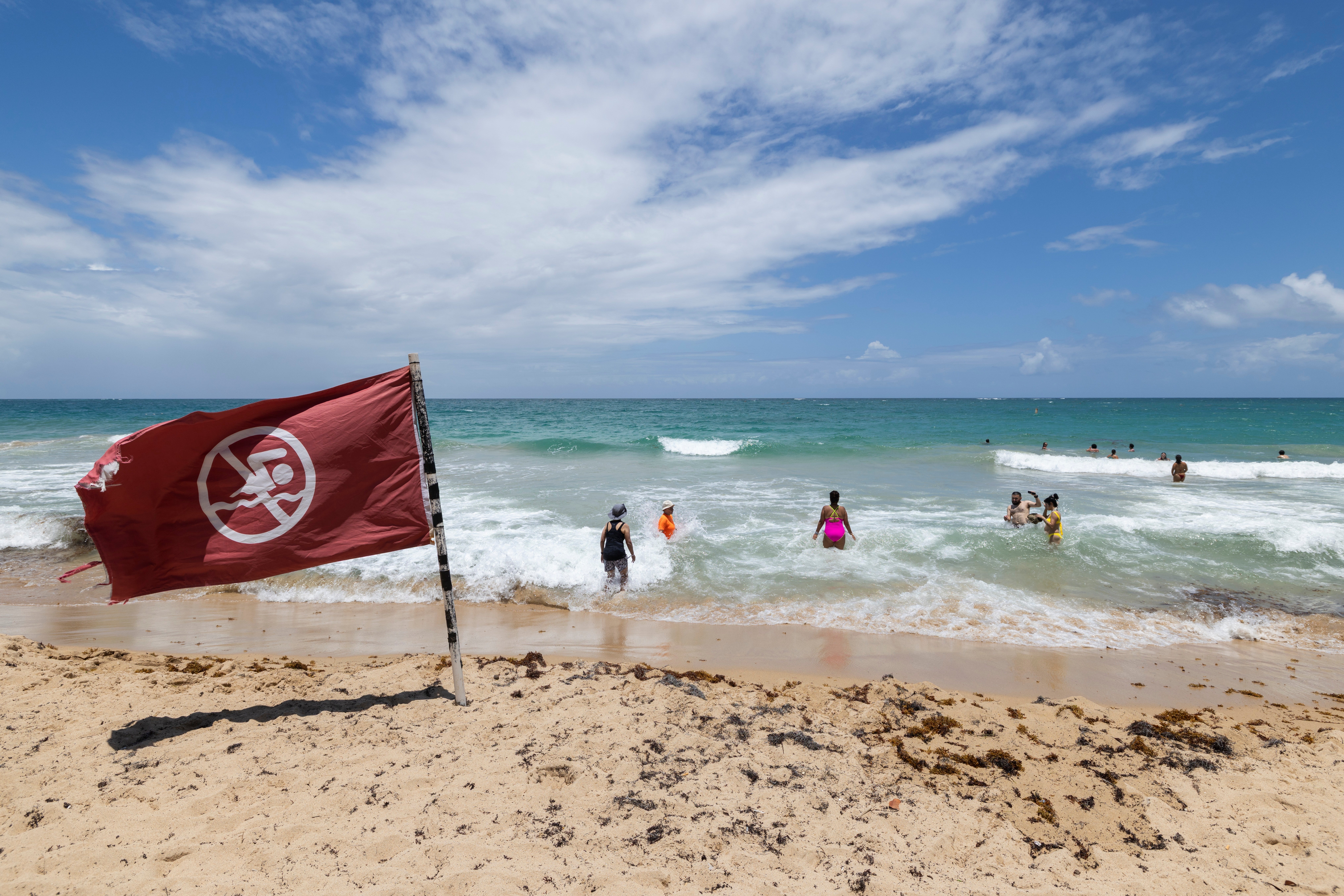 A warning flag flies on the beach as people swim in Condado, Puerto Rico, as Hurricane Erin approaches, Friday, Aug. 15, 2025
