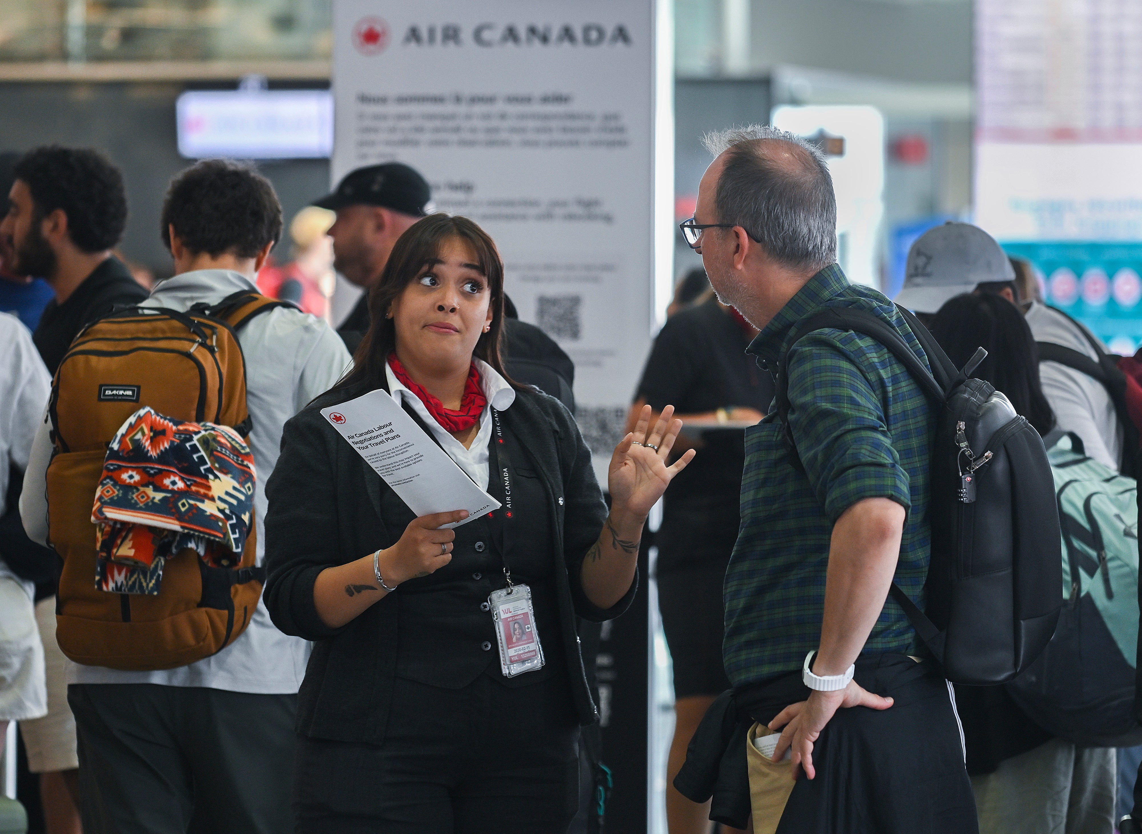 An Air Canada agent, left, talks with a man as Air Canada flight attendants strike at Montreal-Pierre Elliott Trudeau International Airport in Montreal, Saturday, Aug. 16, 2025