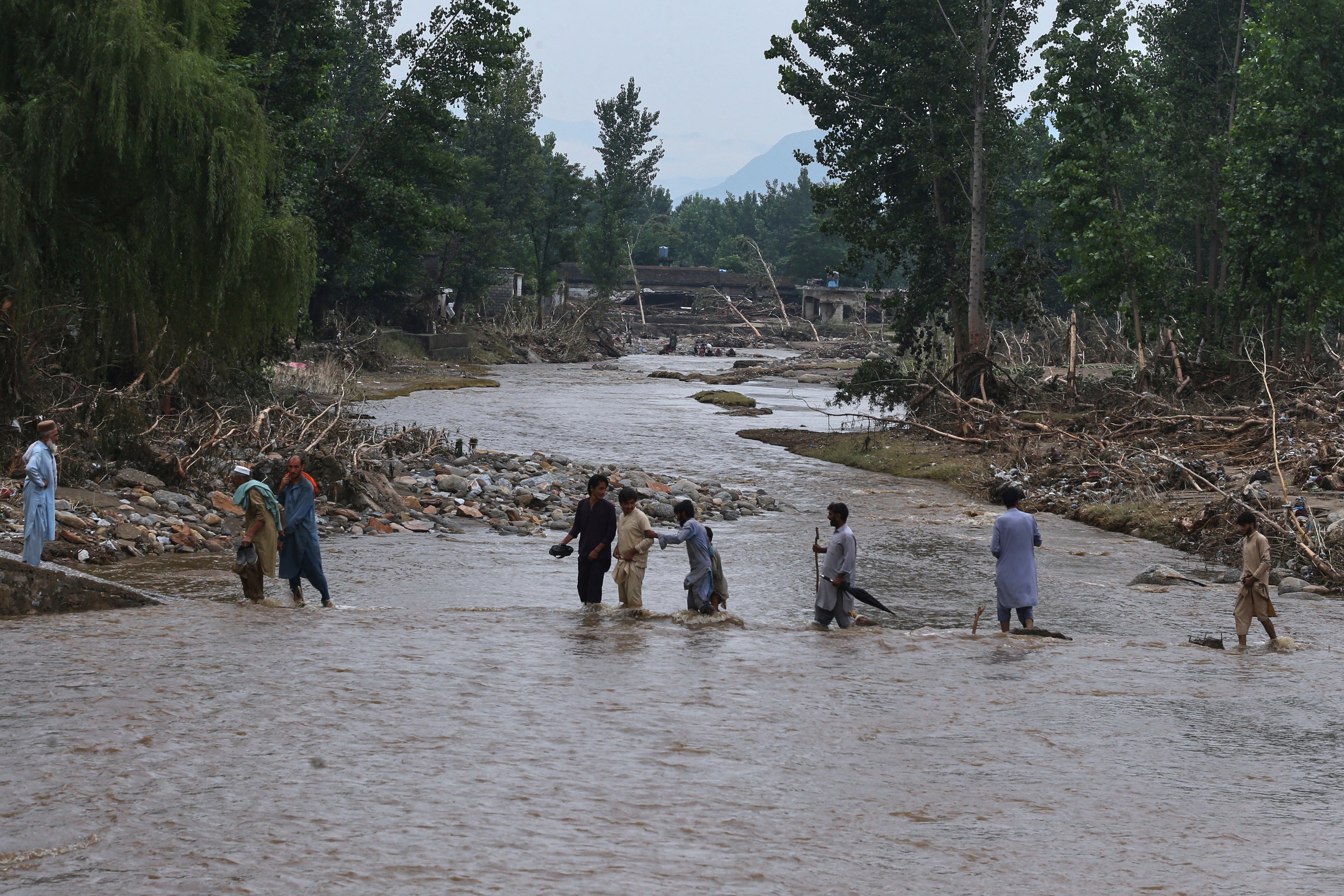 People cross a stream following flash flooding in Buner district in Pakistan