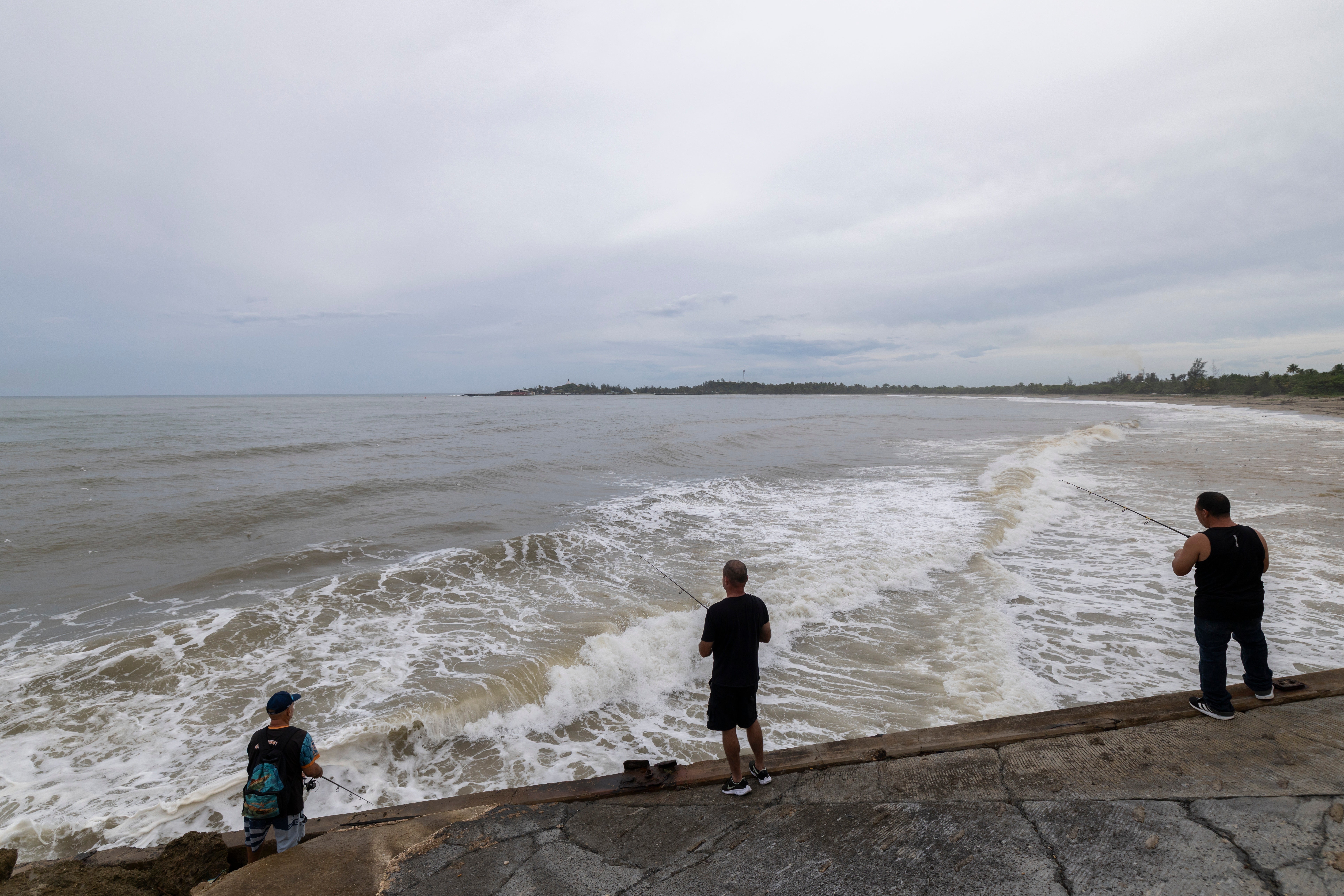 People fish along the shore in Arecibo, Puerto Rico, as Hurricane Erin brings rains to the island