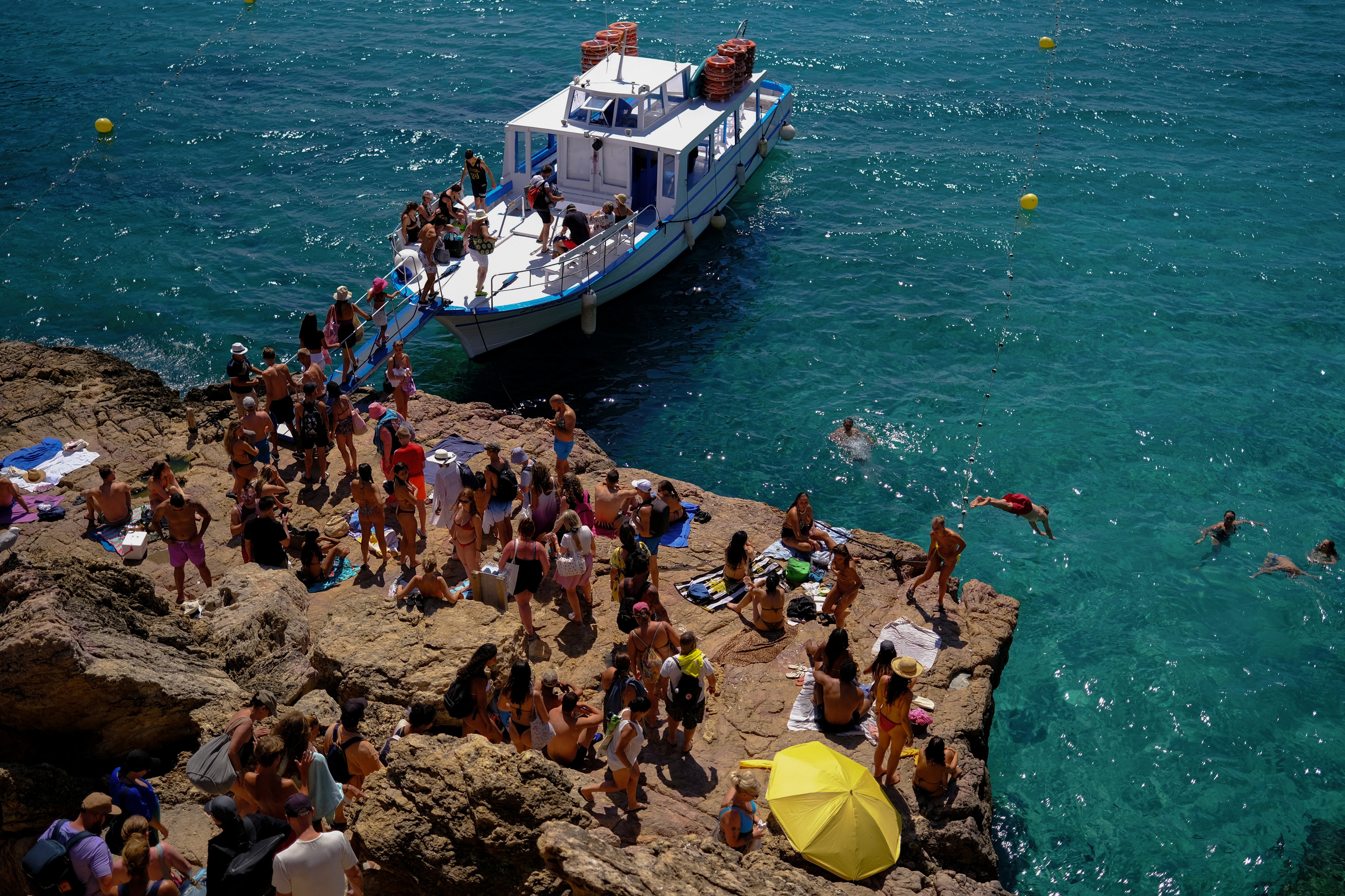 Tourists enjoy the sea as others board a beach touring boat at Cala Saladeta beach in Sant Antoni de Portmany, Ibiza