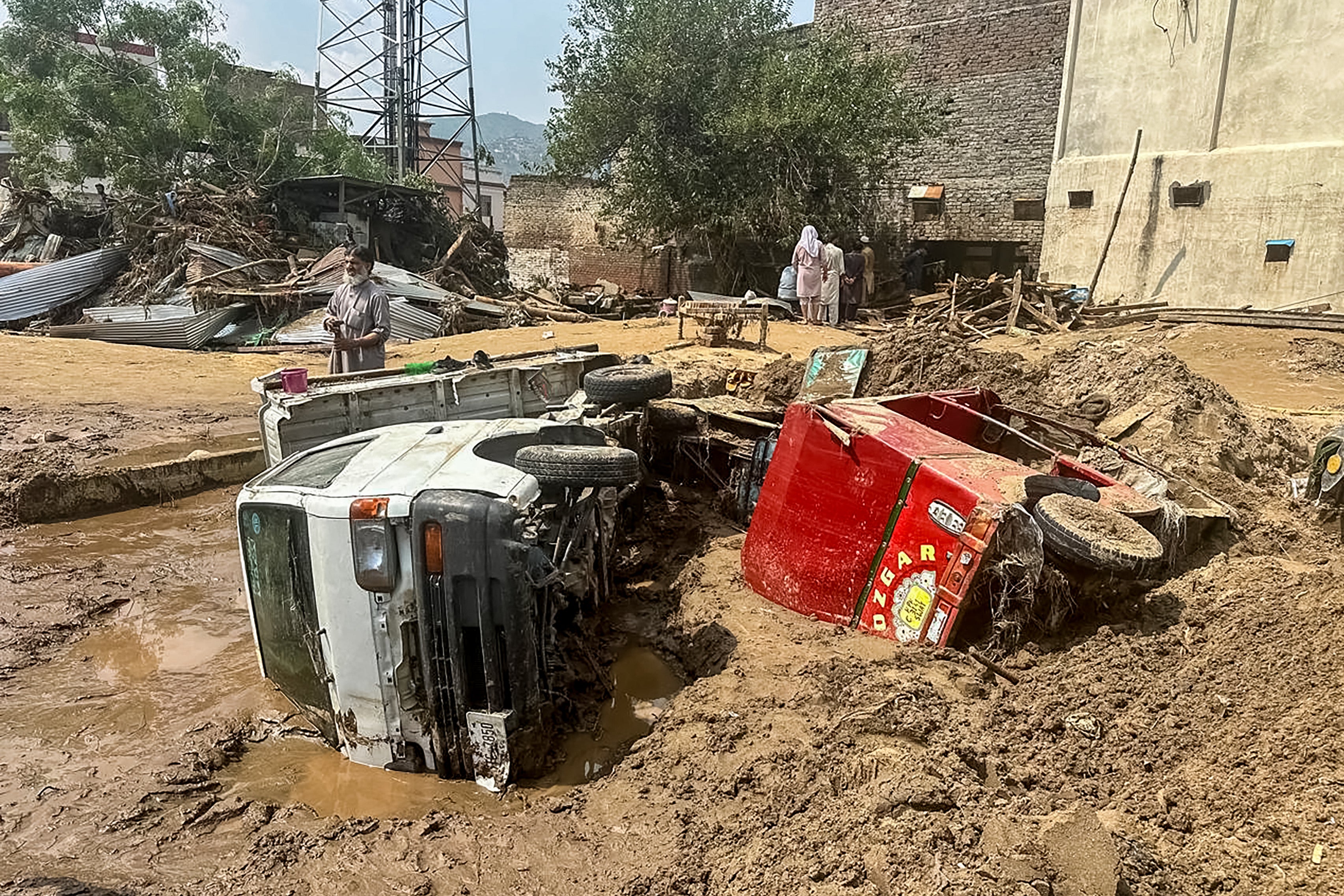 People walk past damaged vehicles and scattered debris following a flash flood in Mingora, the main city of Swat, Pakistan
