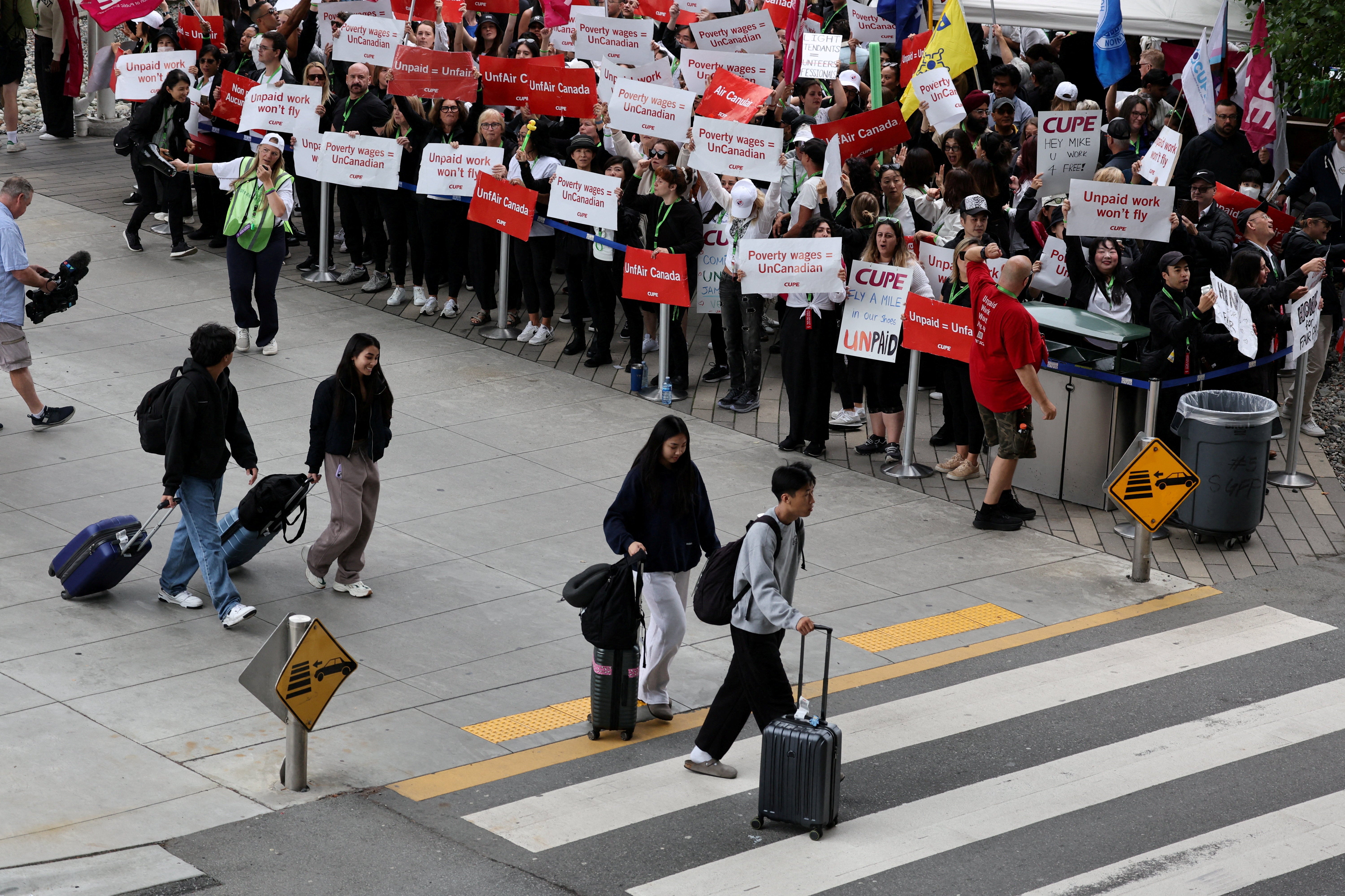 Passengers walk in front of demonstrators holding placards as Air Canada flight attendants said they will remain on strike and challenge a return-to-work order they called unconstitutional