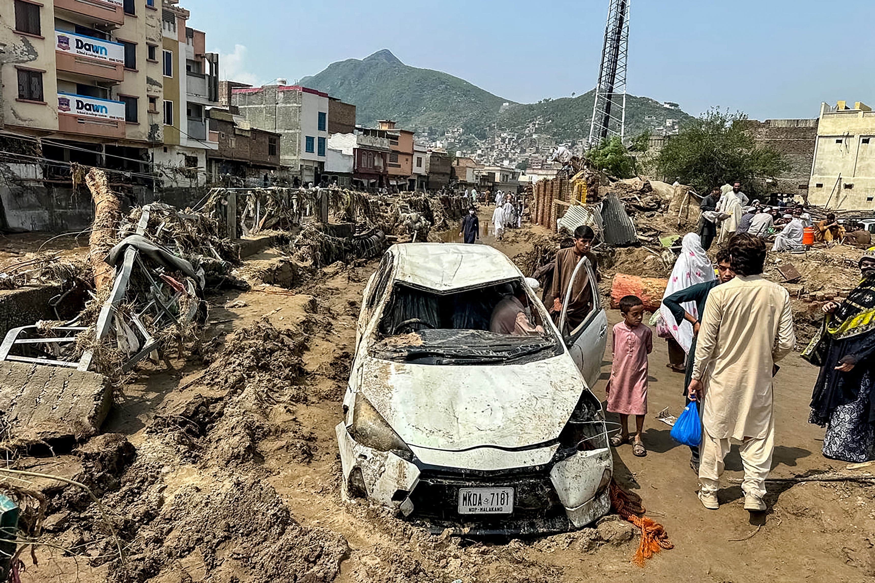 People gather near a damaged vehicle and scattered debris after the road washed out following a flash flood in Mingora, the main city of Swat Valley, in monsoon-hit northern Pakistan's mountainous Khyber Pakhtunkhwa province