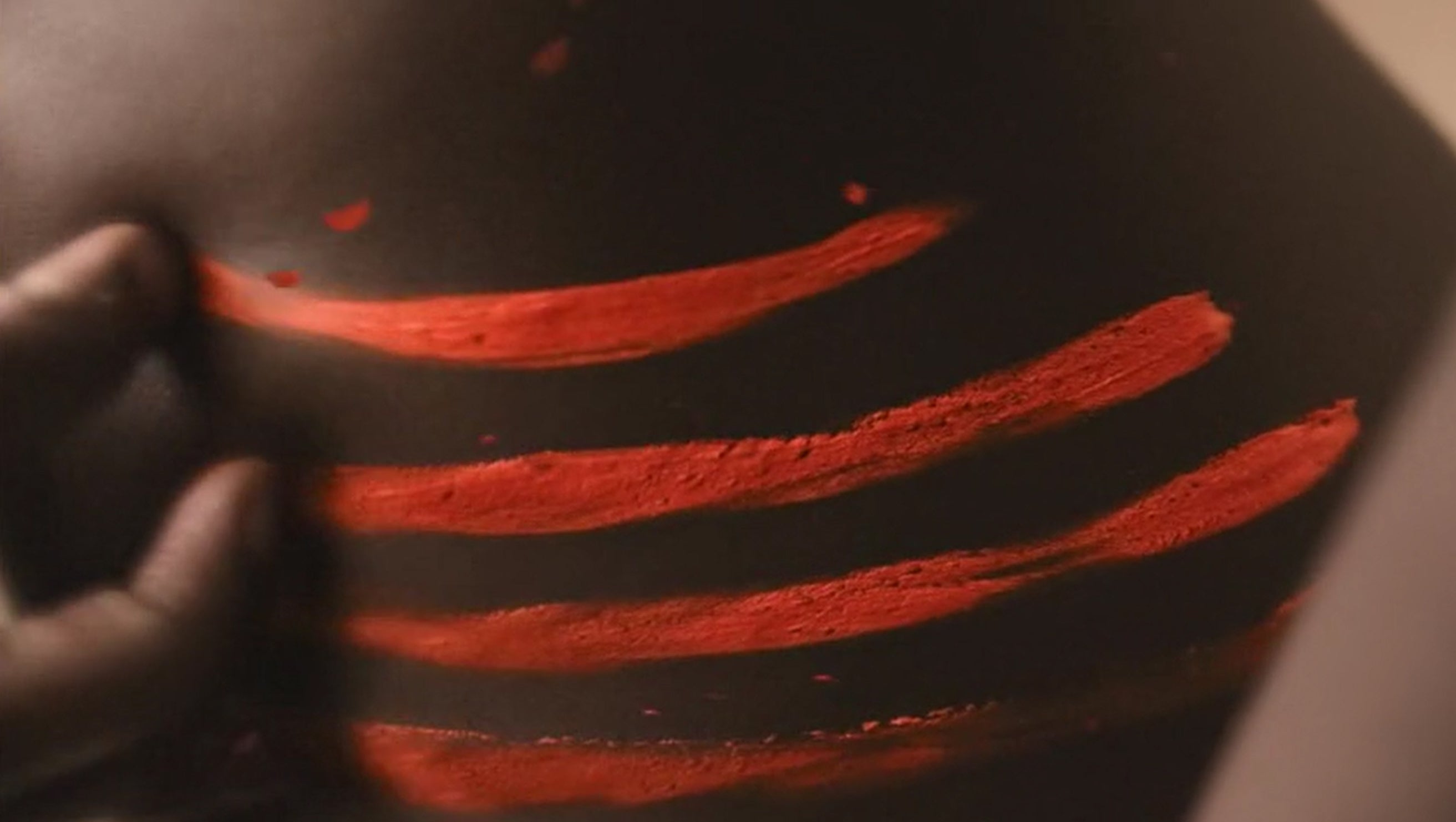 In another scene, a Black woman is shown with red scratch marks over their body