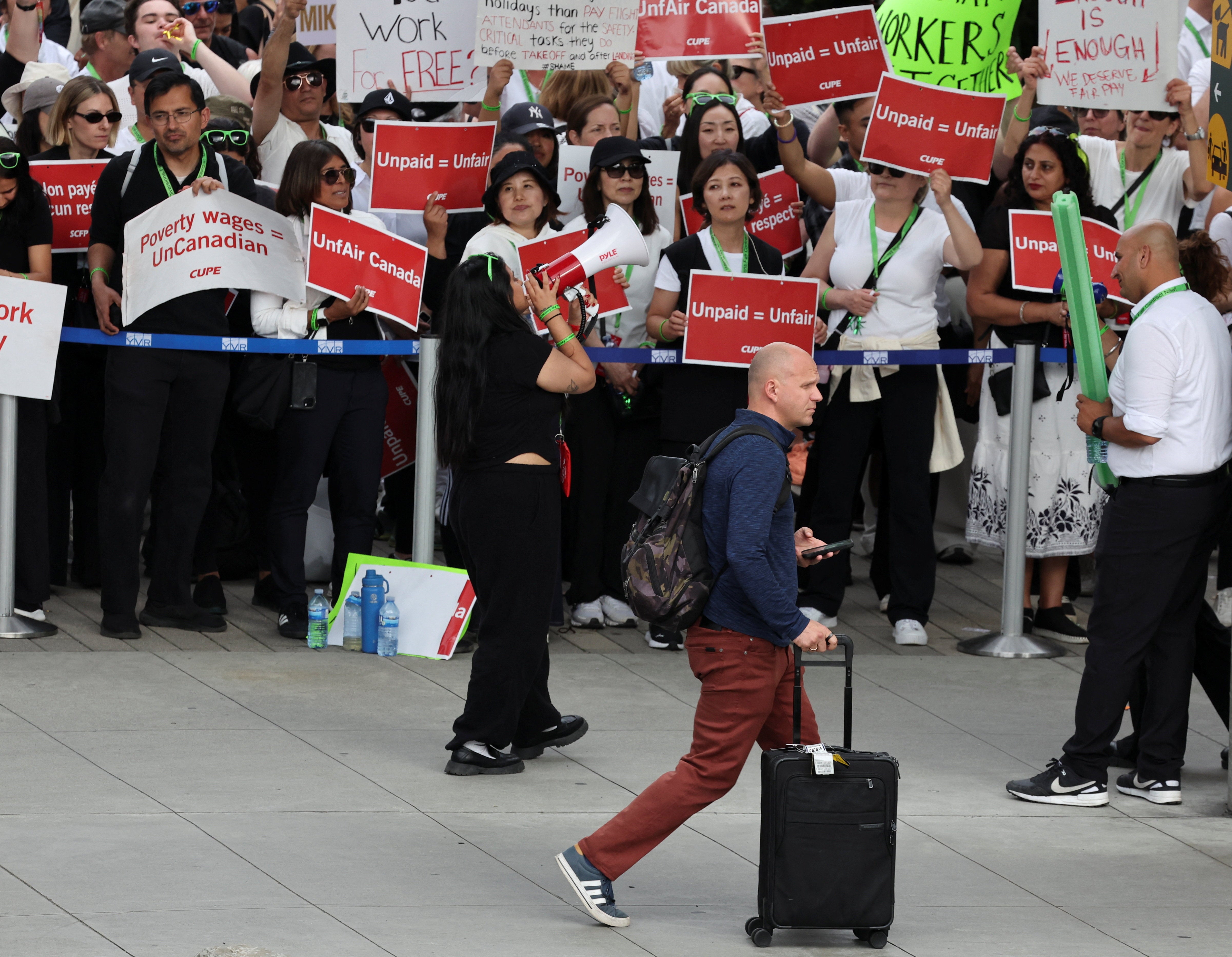 A passenger walks as striking Air Canada flight attendants hold placards as they defy a back to work order at Vancouver International Airport in Richmond, British Columbia, Canada