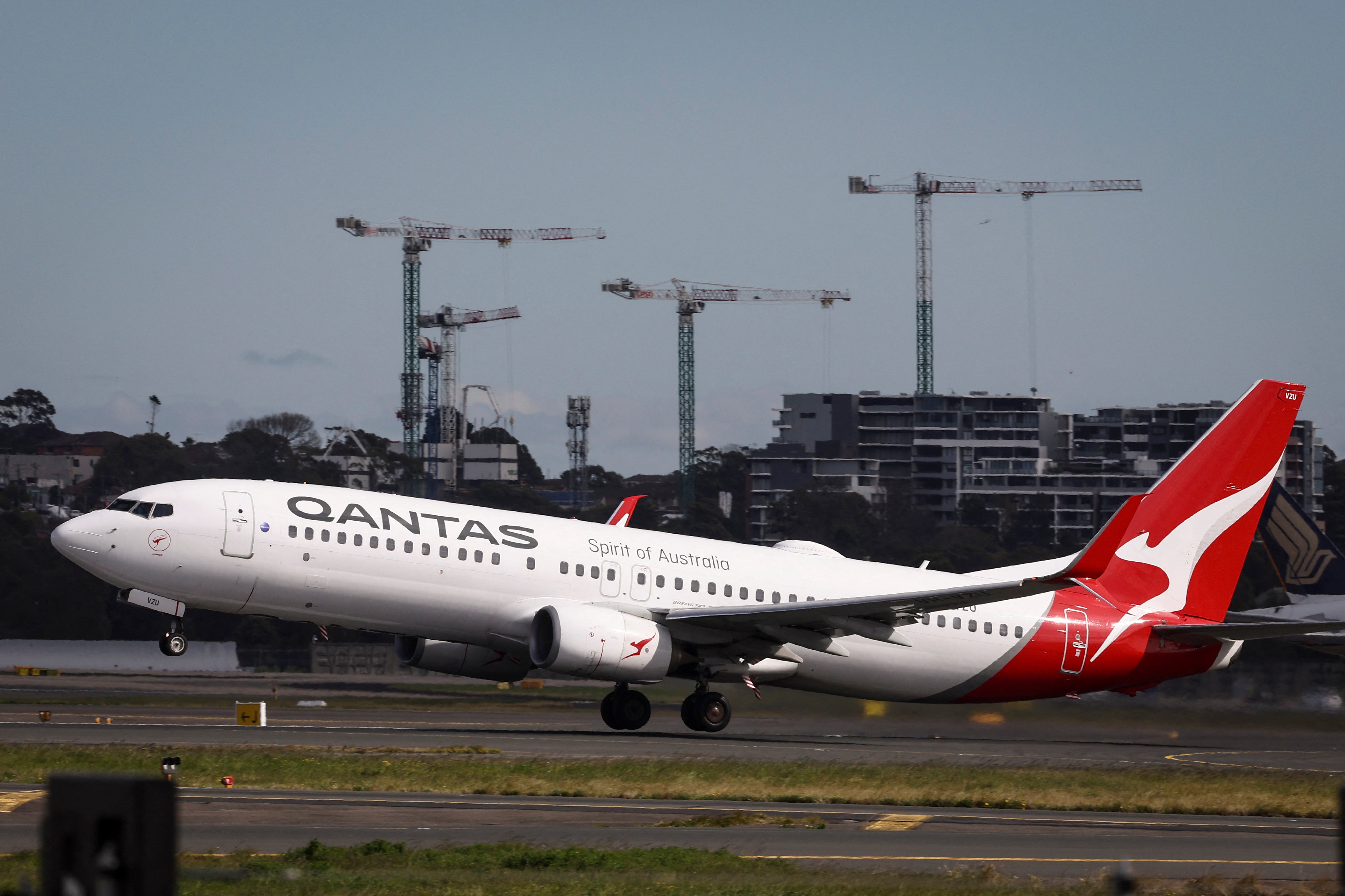 Cranes on a construction site are seen behind a Qantas Airways Boeing 737 aircraft as it takes off from Sydney International Airport