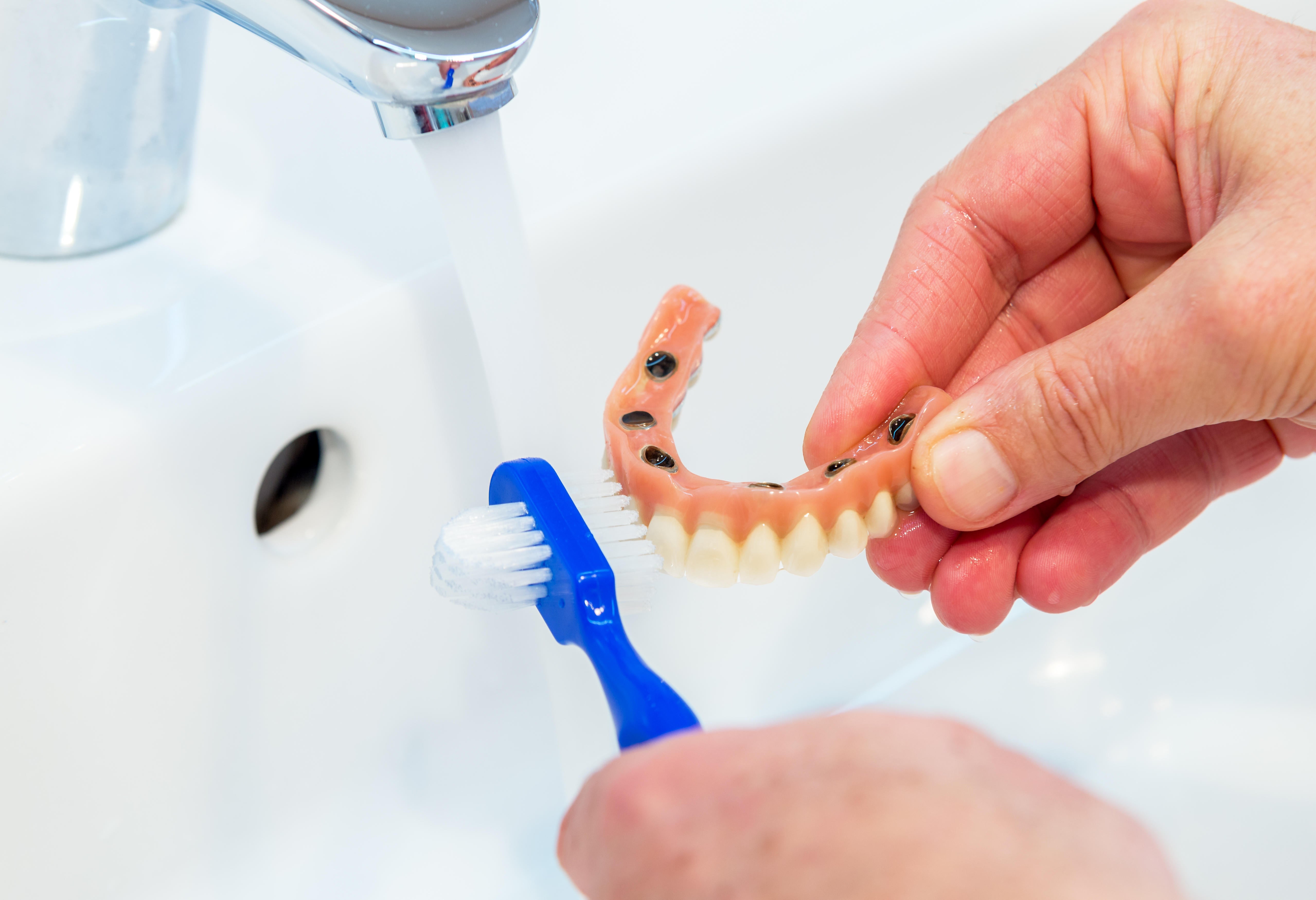 Close up picture of hands brushing dentures clean in a sink