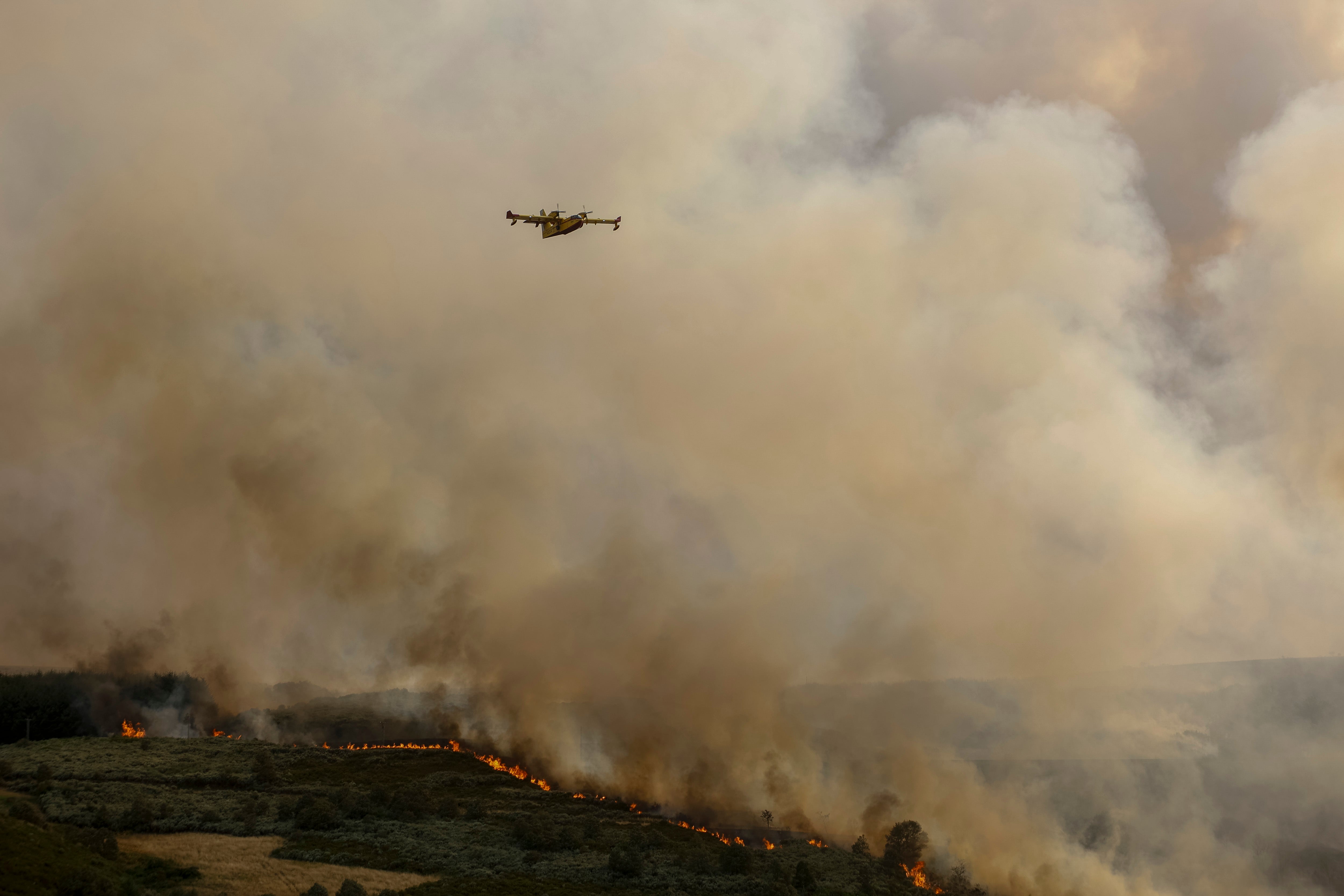 A firefighter aircraft flies over flames during a wildfire on August 18, 2025 in A Goudiña