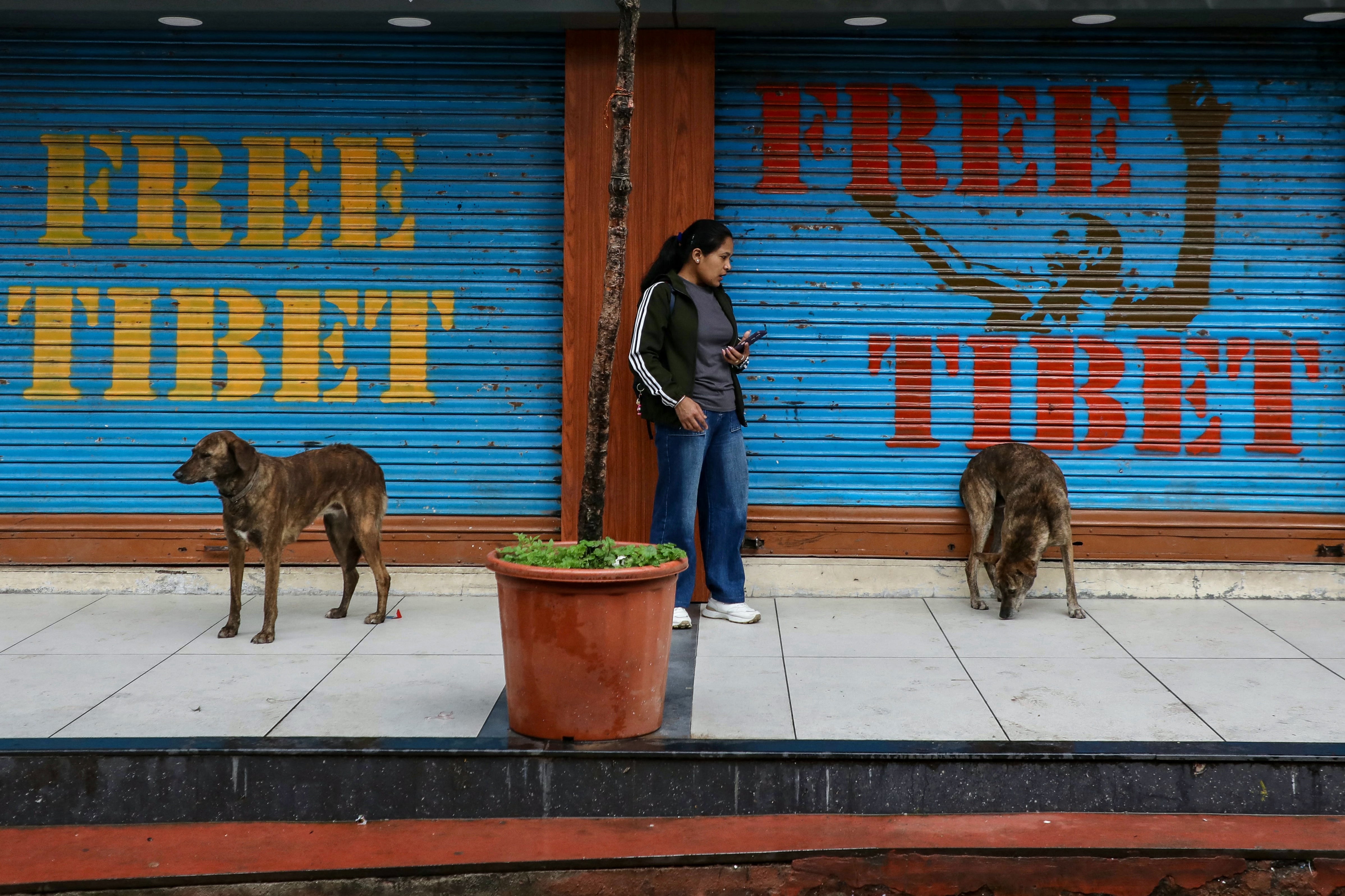 A woman stands next to closed shops displaying the slogan ‘Free Tibet’ on a rainy day in a suburb near Dharamsala, on 4 July 2025