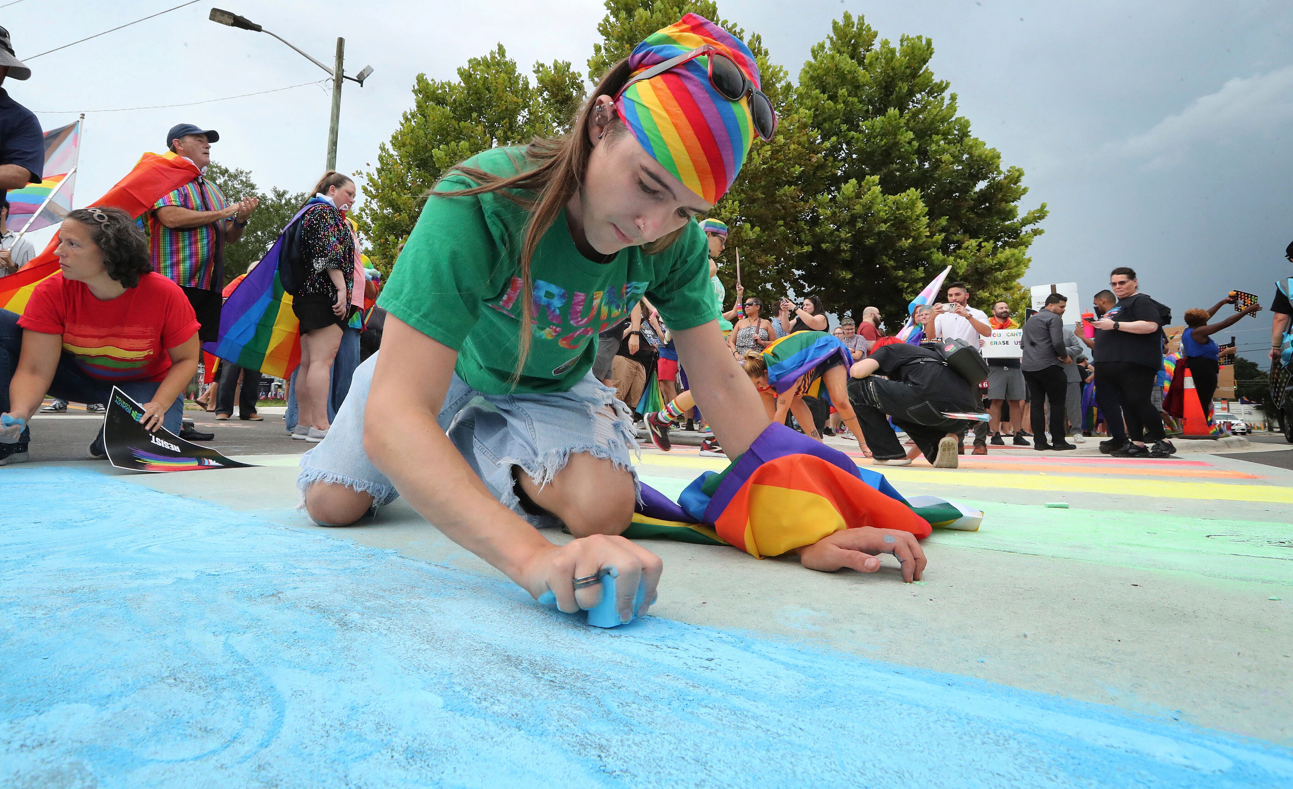 A demonstrator uses blue chalk to color the street during a protest at a crosswalk that was repainted by the Florida Department of Transportation