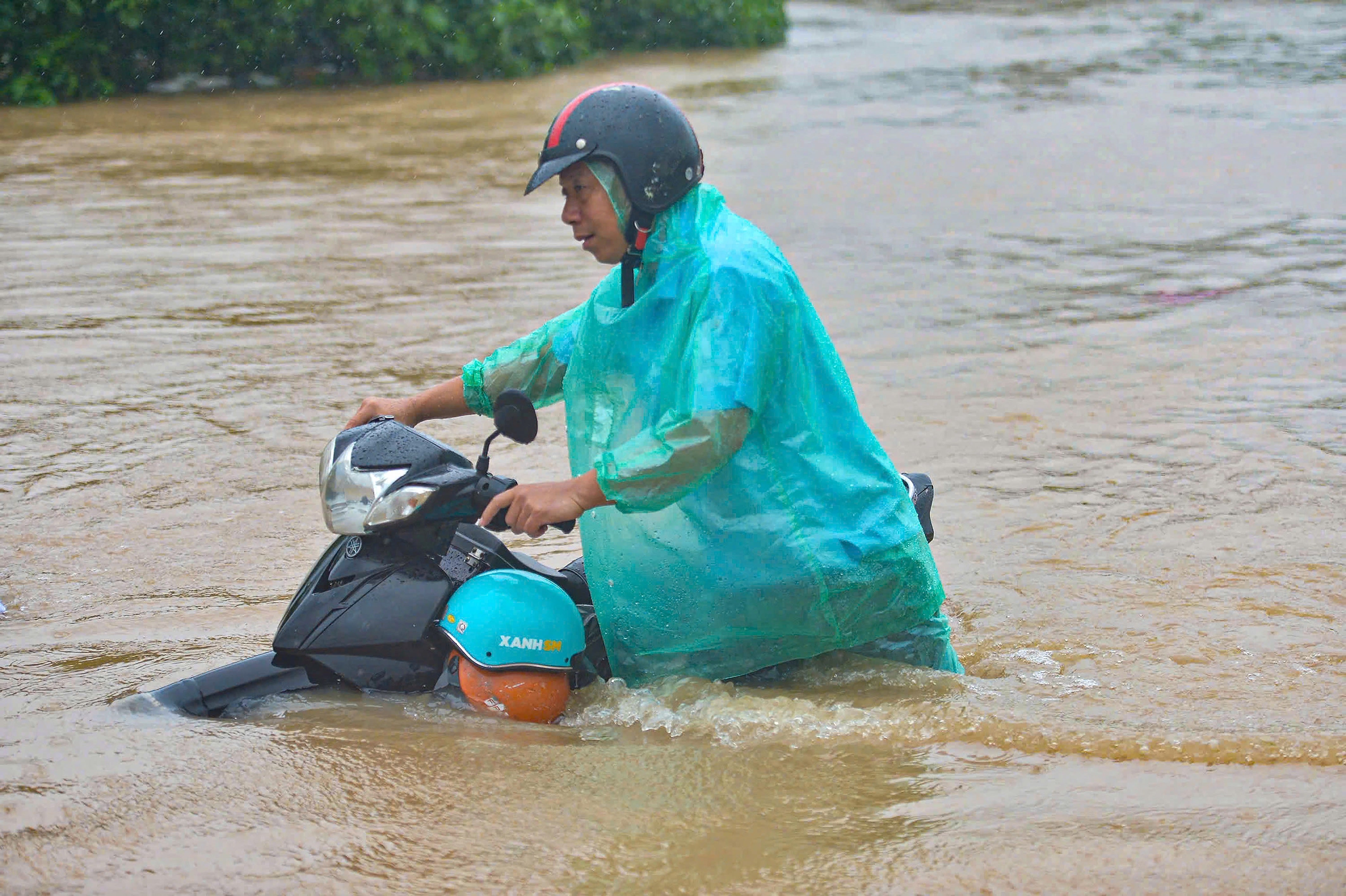 A man pushes a motorbike through a flooded street following the passage of Typhoon Kajiki in Hanoi