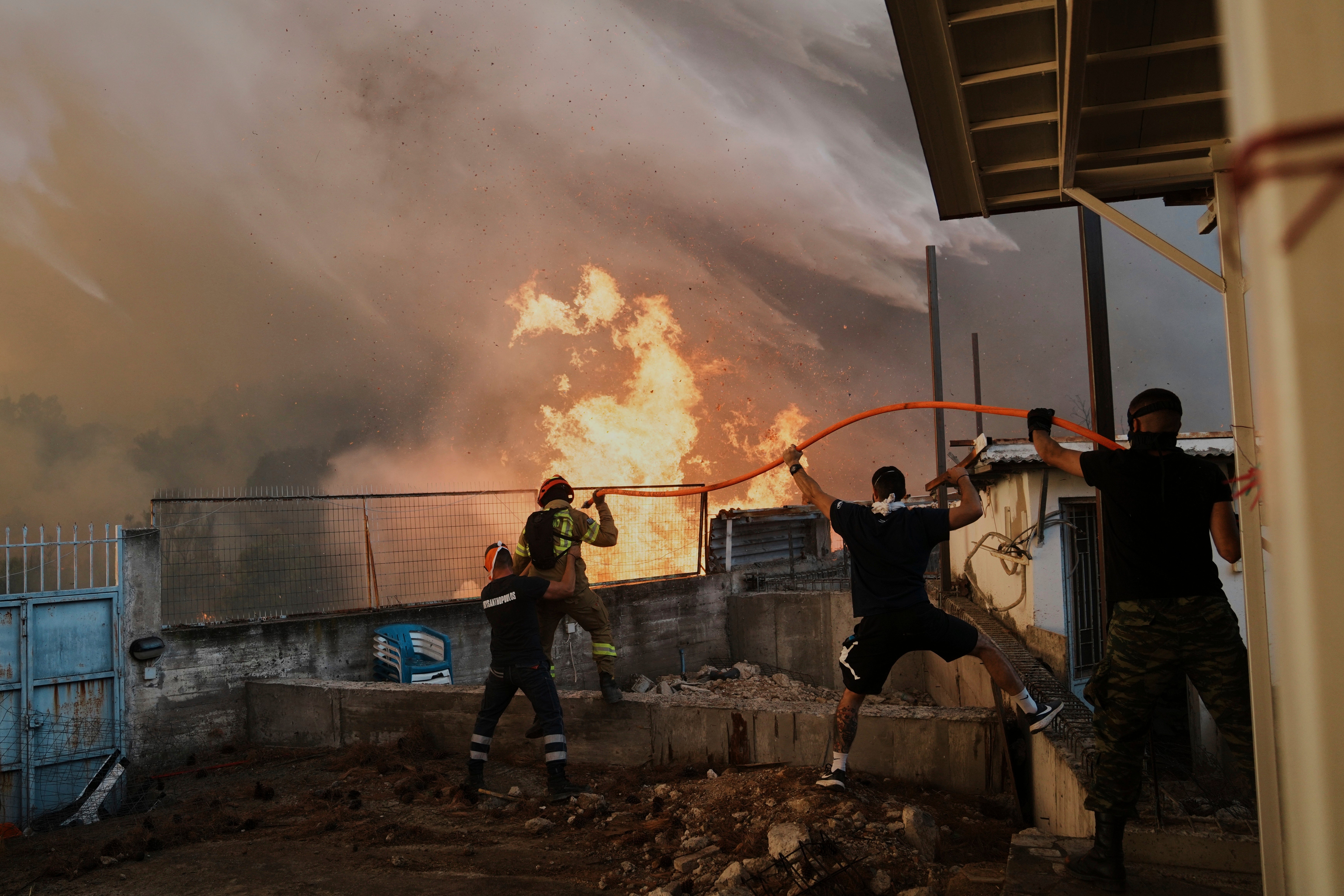 A firefighter and men try to control the flames approaching a house during a wildfire in Patras city