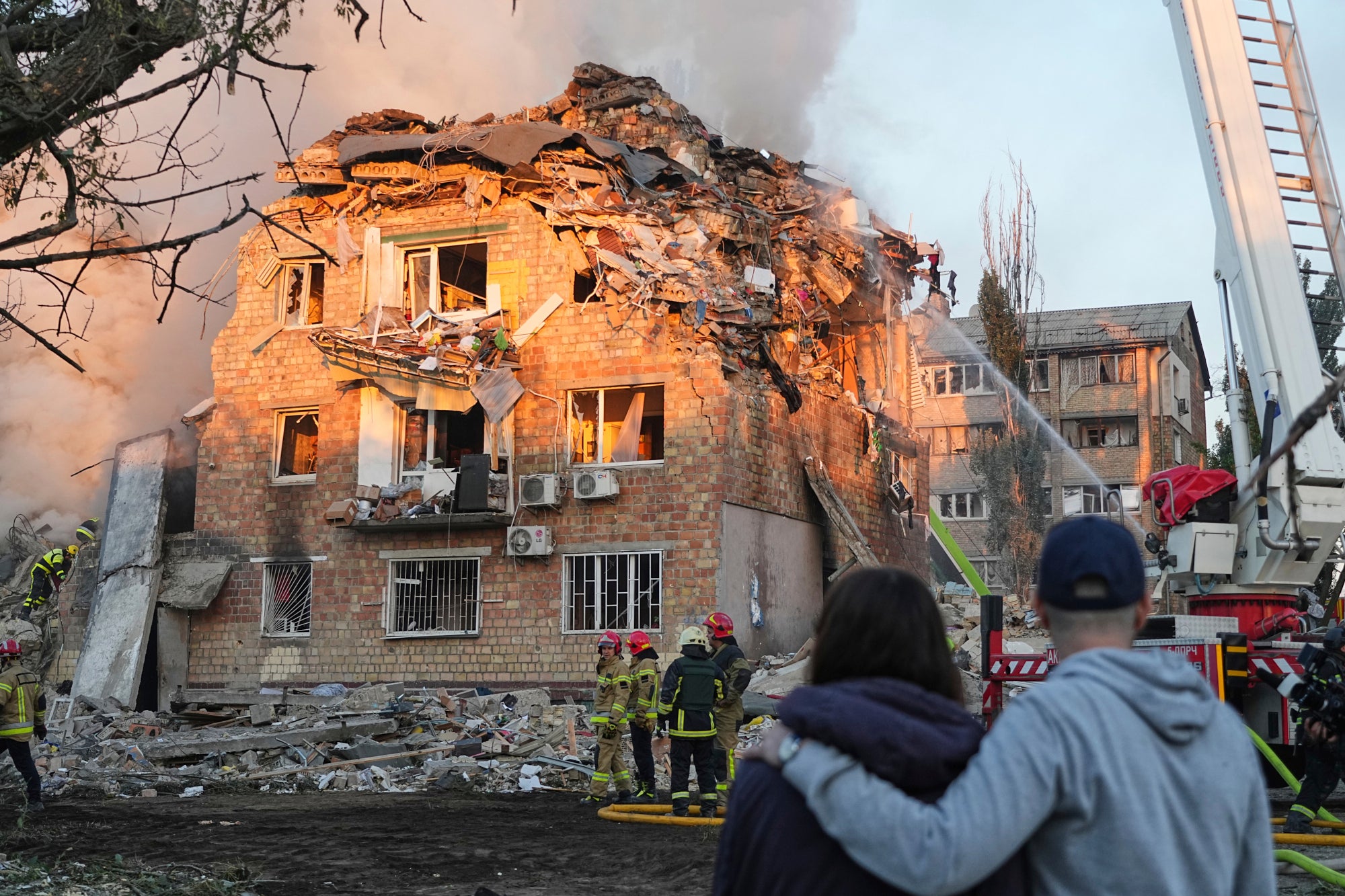 Residents watch on as fire crews tackle flames at a building hit by strikes