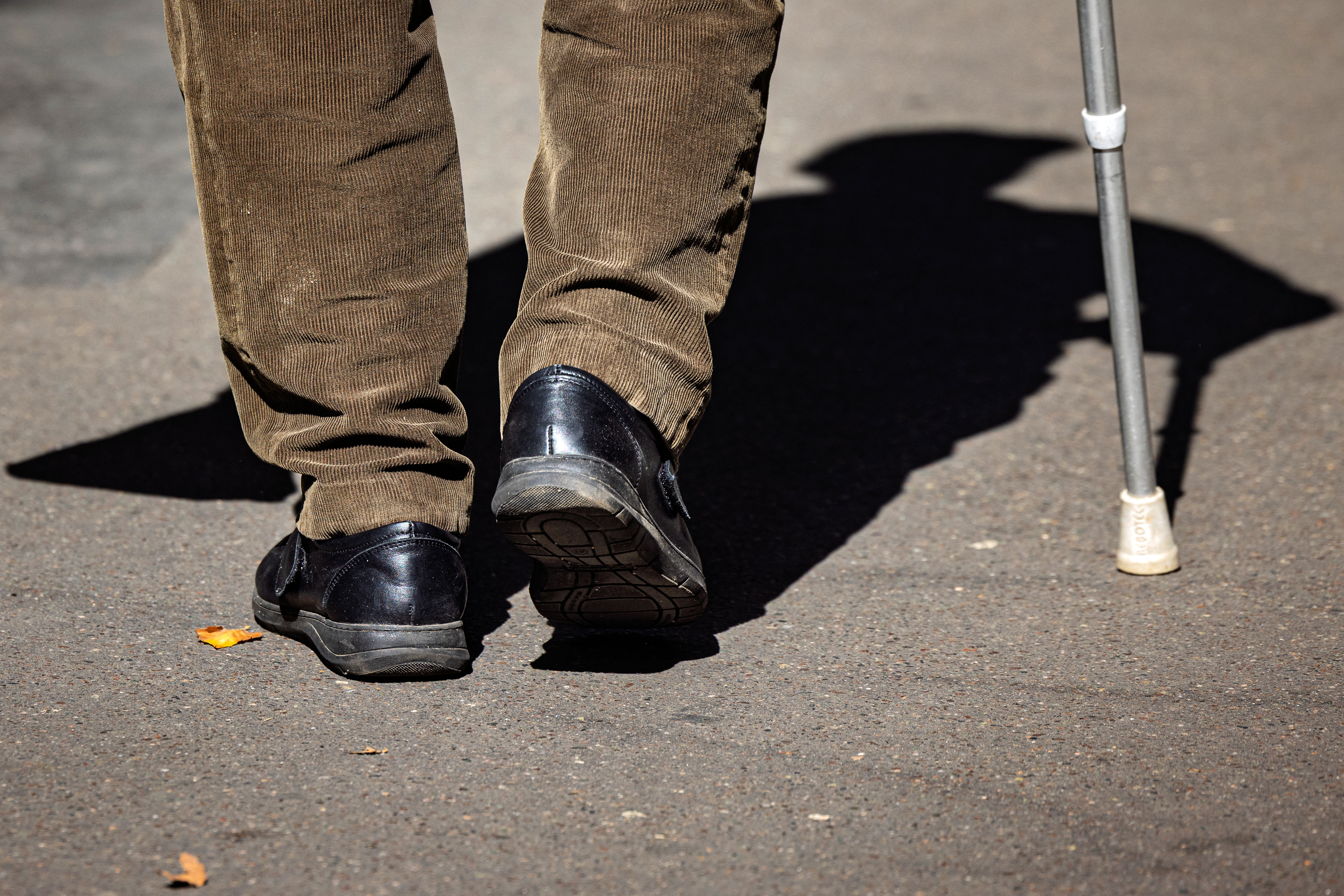 An elderly person walks with a cane along a Paris sidewalk