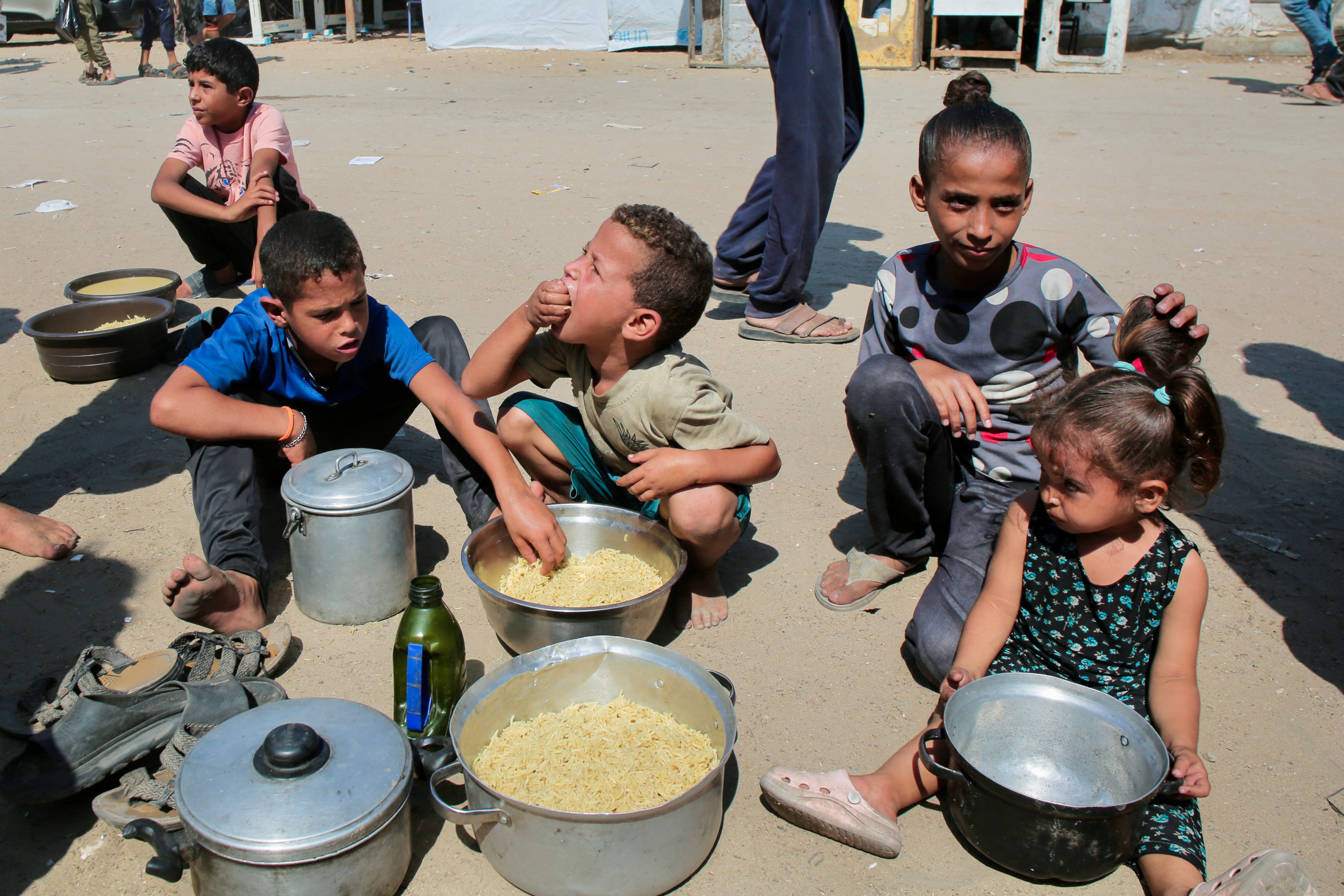 Palestinian children eat cooked rice after managing to get portions of hot food from a charity kitchen in Khan Yunis