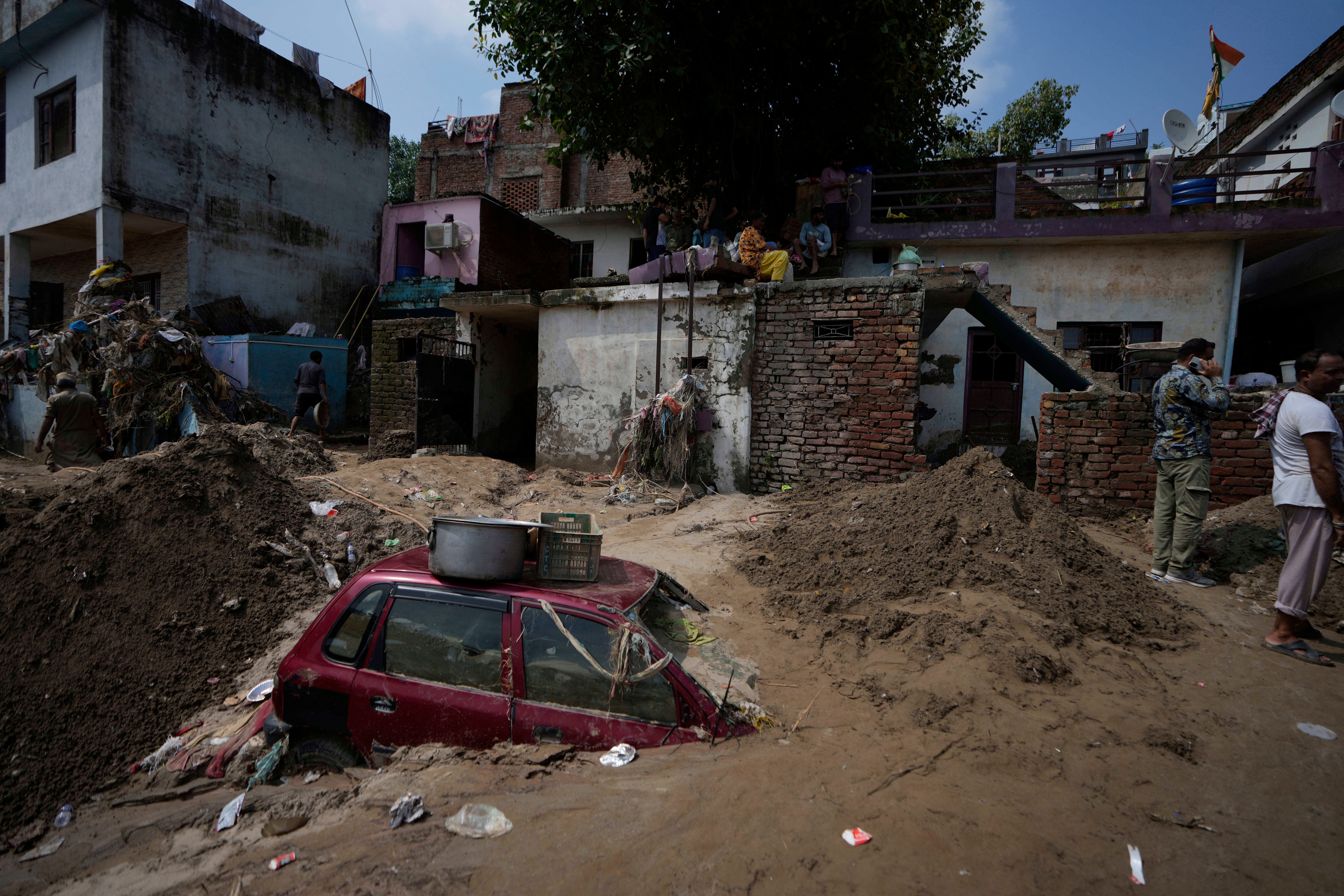 People clear mud from their home following flash floods along the banks of the Tawi river in Jammu