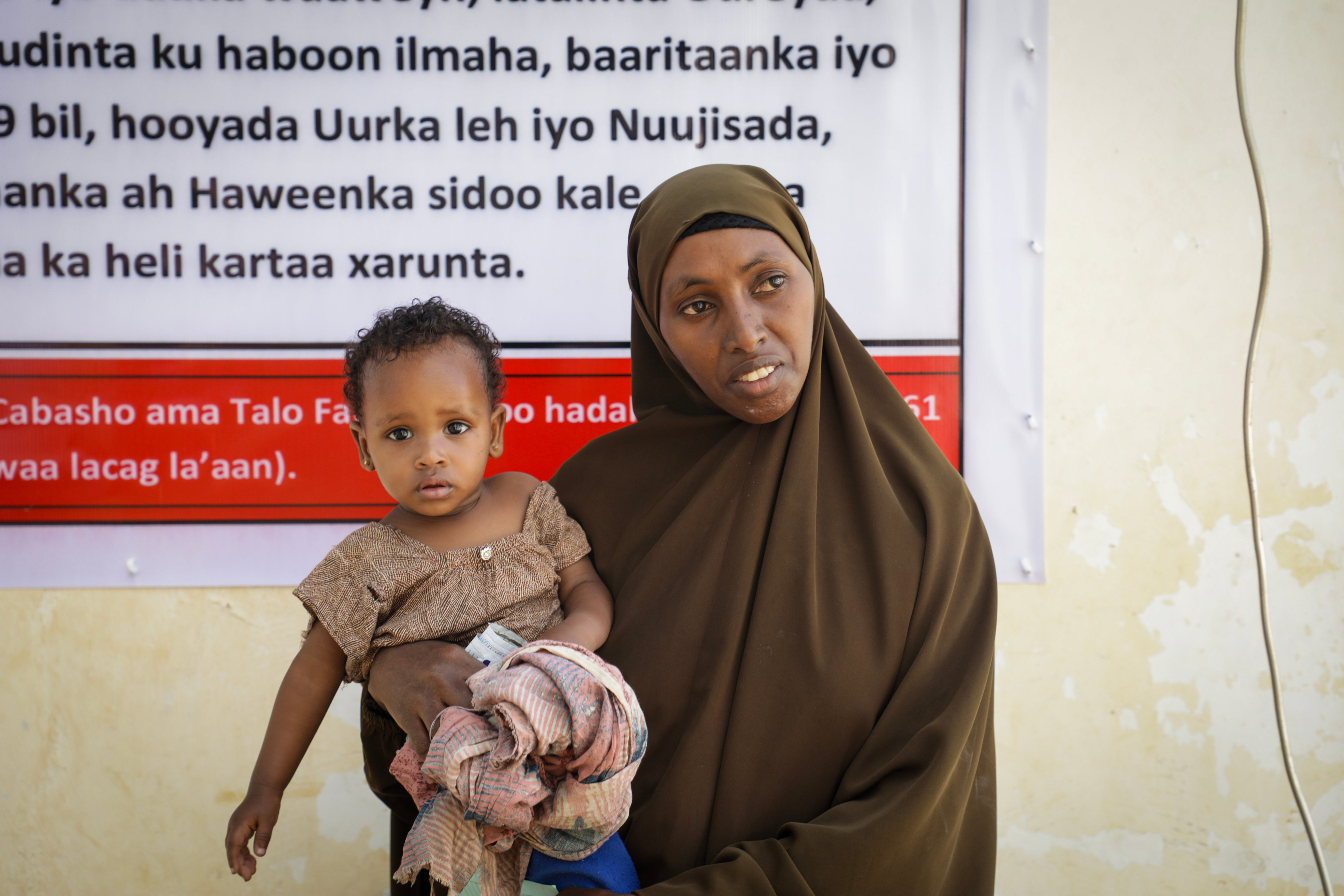 Dahaboo, 38 stands for a portrait with her baby Aaden, one, at a nutrition centre in Baidoa, Somalia. Nutrition centres such as this are under threat across Africa due to aid cuts