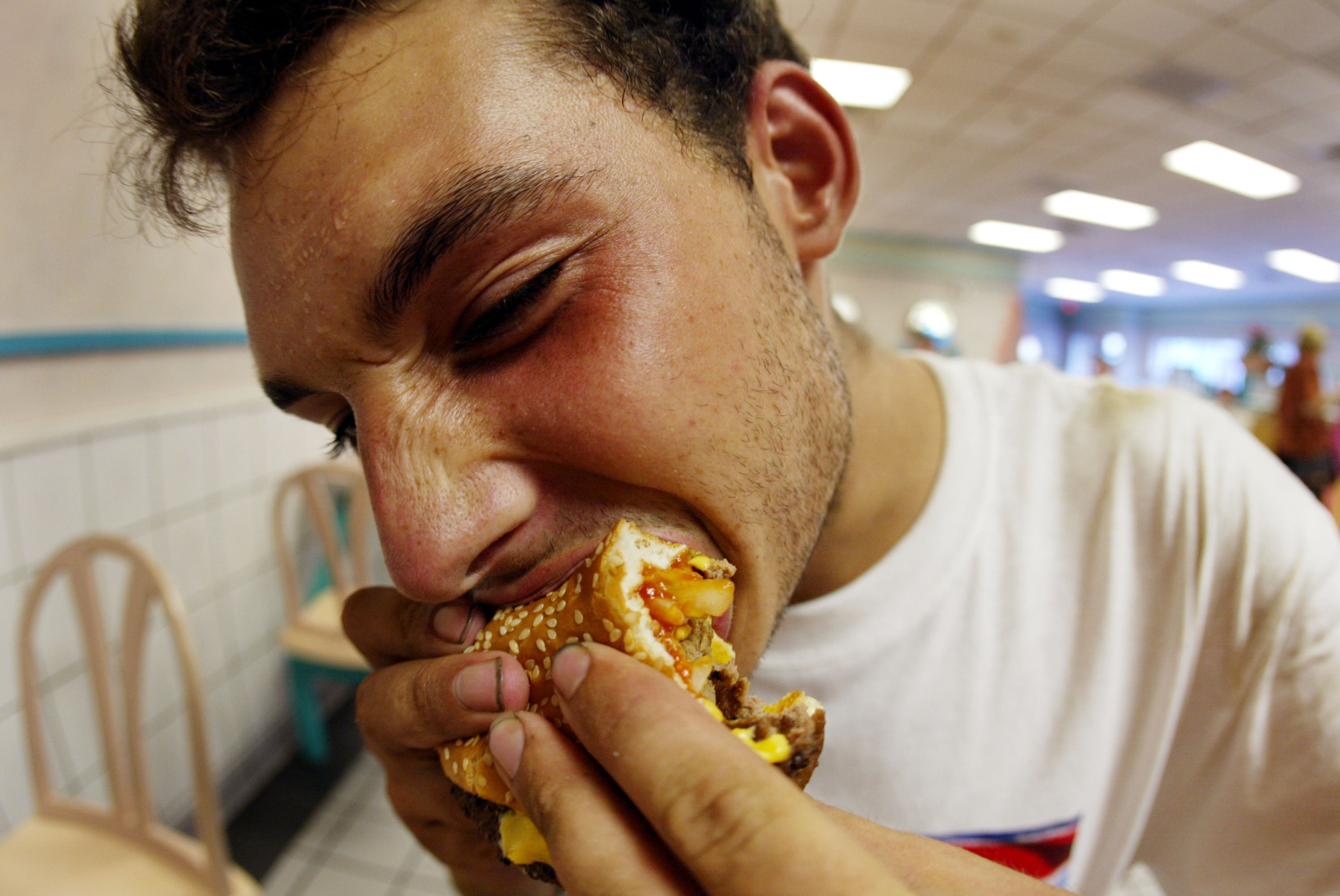Muž kousne do dvojitého cheeseburgeru. Jíst ultraprocesované potraviny mohou ovlivnit reprodukční zdraví mužů, uvedli vědci tento týden