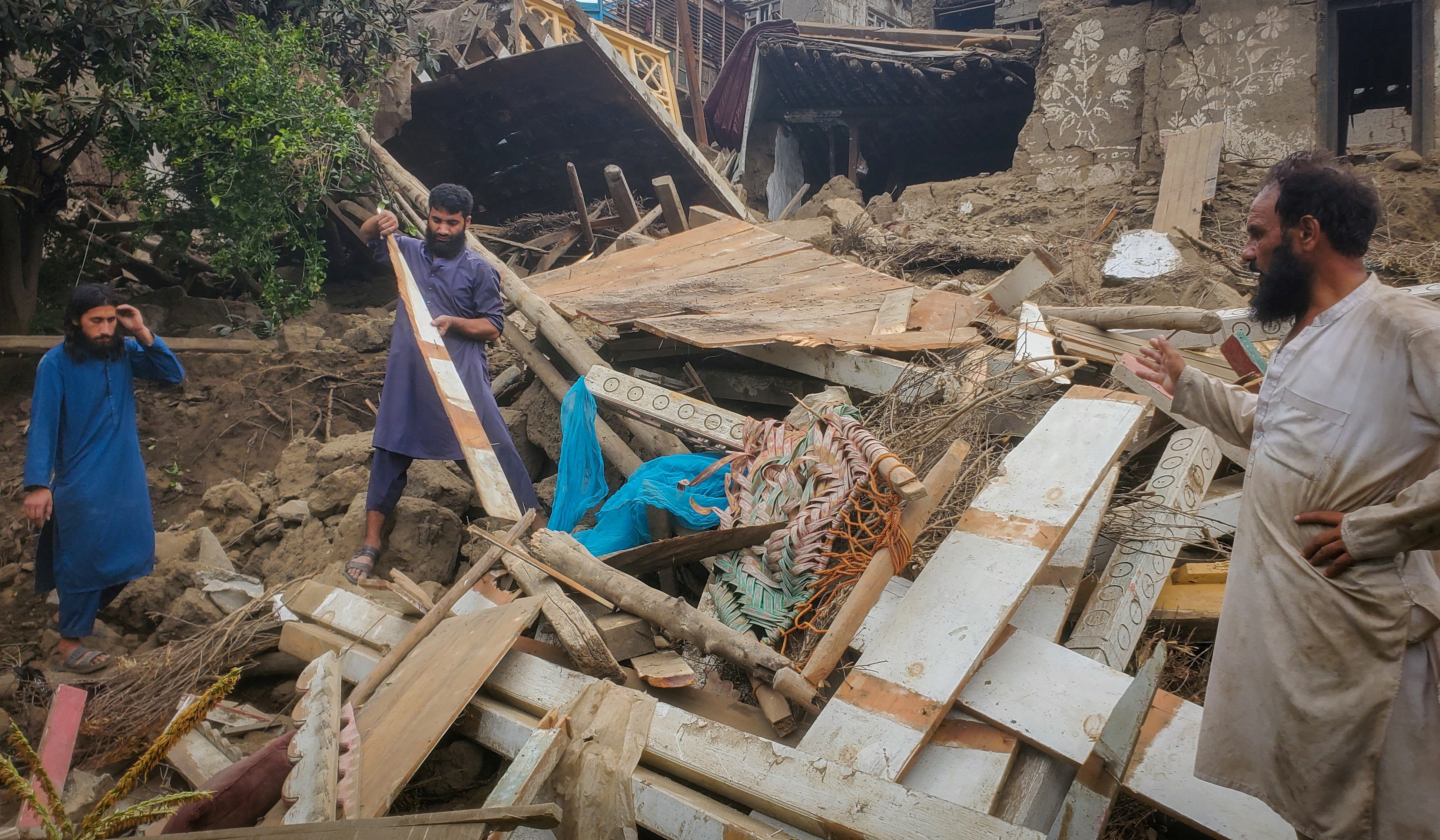 Afghan men search for their belongings in the rubble of a collapsed house