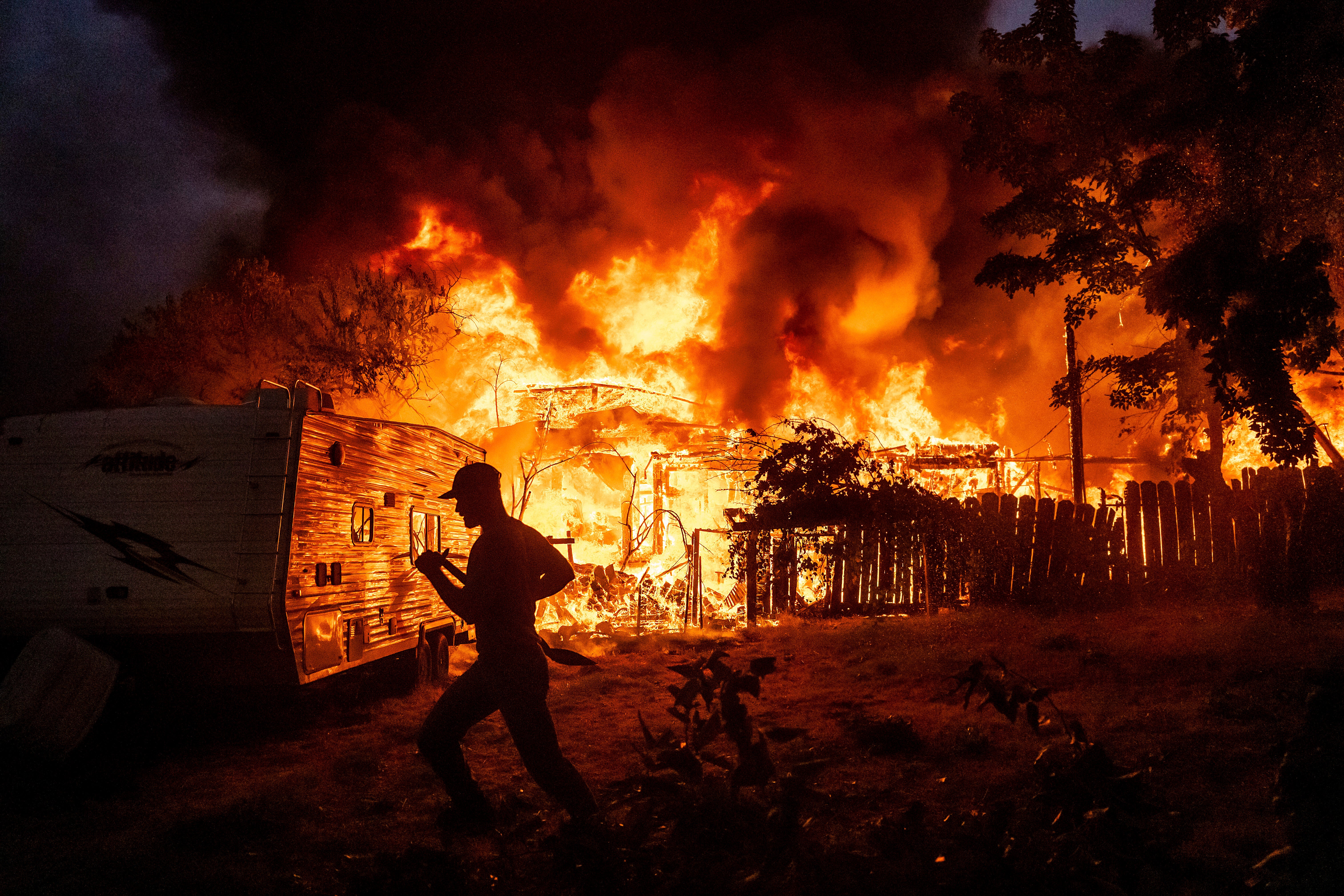 A residents works to stop flames from a burning home from spreading to a neighboring house as the 6-5 Fire burns through the Chinese Camp community of Tuolumne County, Calif., on Tuesday, Sept. 2, 2025. (AP Photo/Noah Berger)