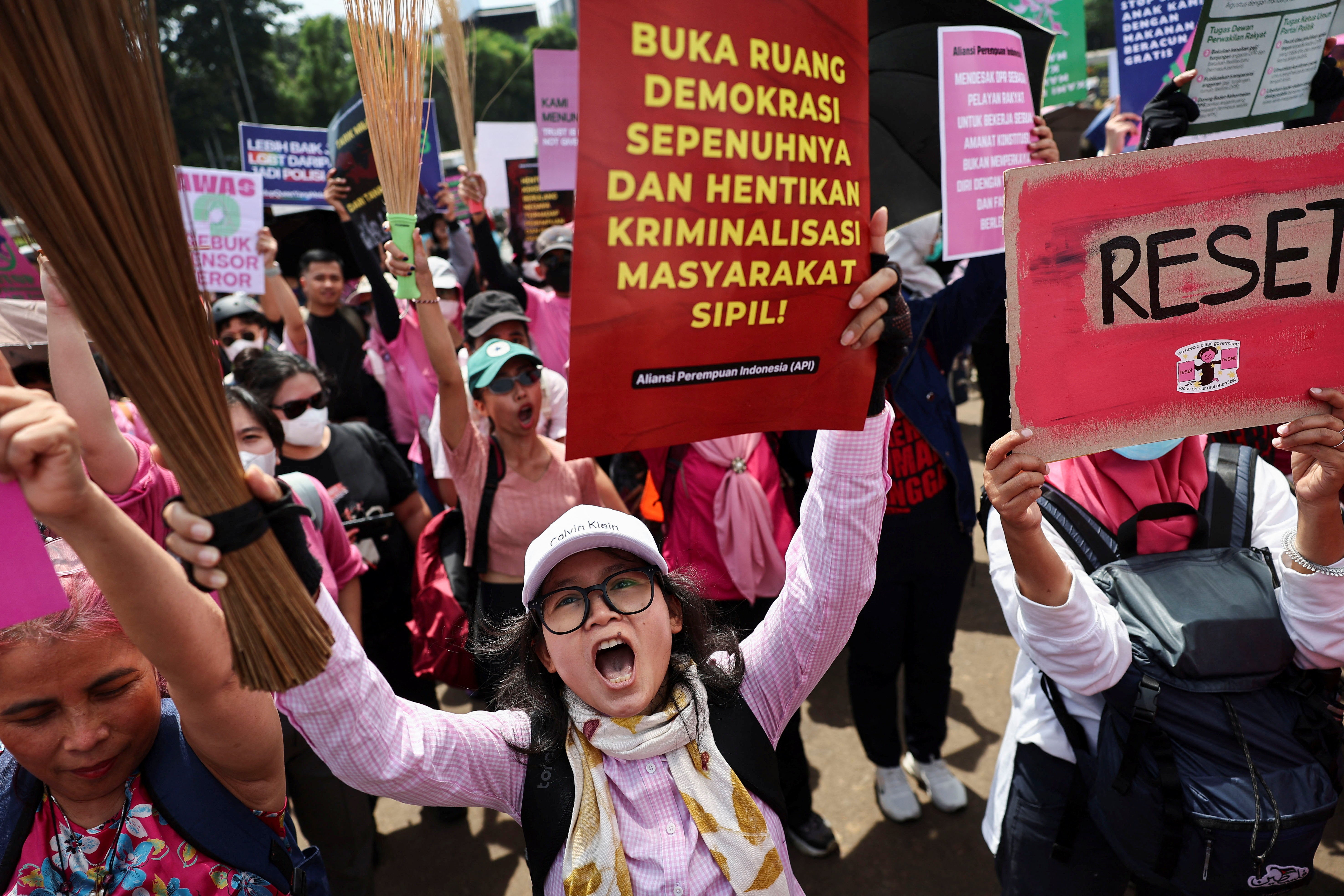 Women holding up brooms and placards shout slogans during a protest against lawmakers' perks and police brutality, brandishing brooms as a symbol of their calls for reform