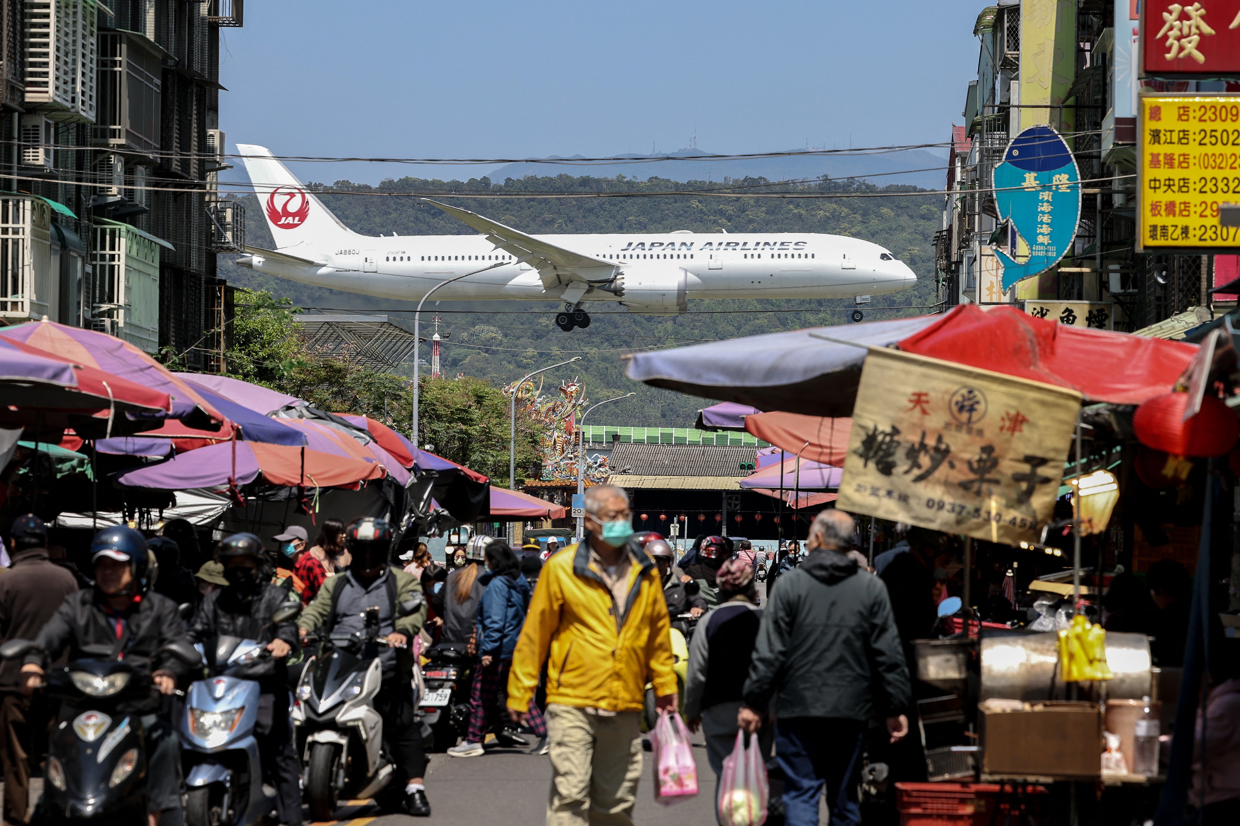 A Japan Airlines plane lands as people visit a market in Taipei on 20 March 2025