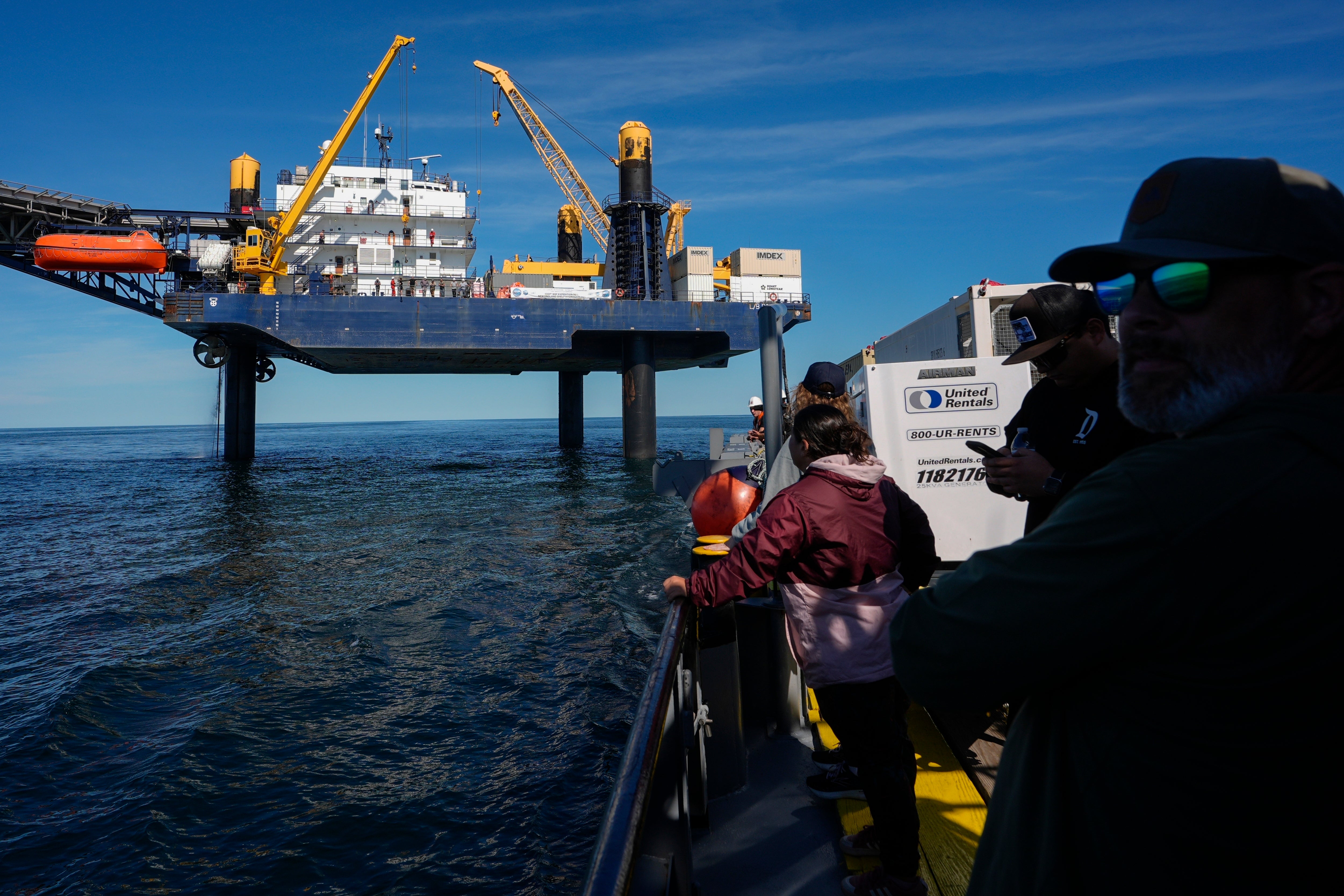 Expedition 501 members look down from the Liftboat Robert platform, to the approaching Gaspee, a crew transport vessel, in the North Atlantic, Saturday, July 19, 2025. (AP Photo/Carolyn Kaster)