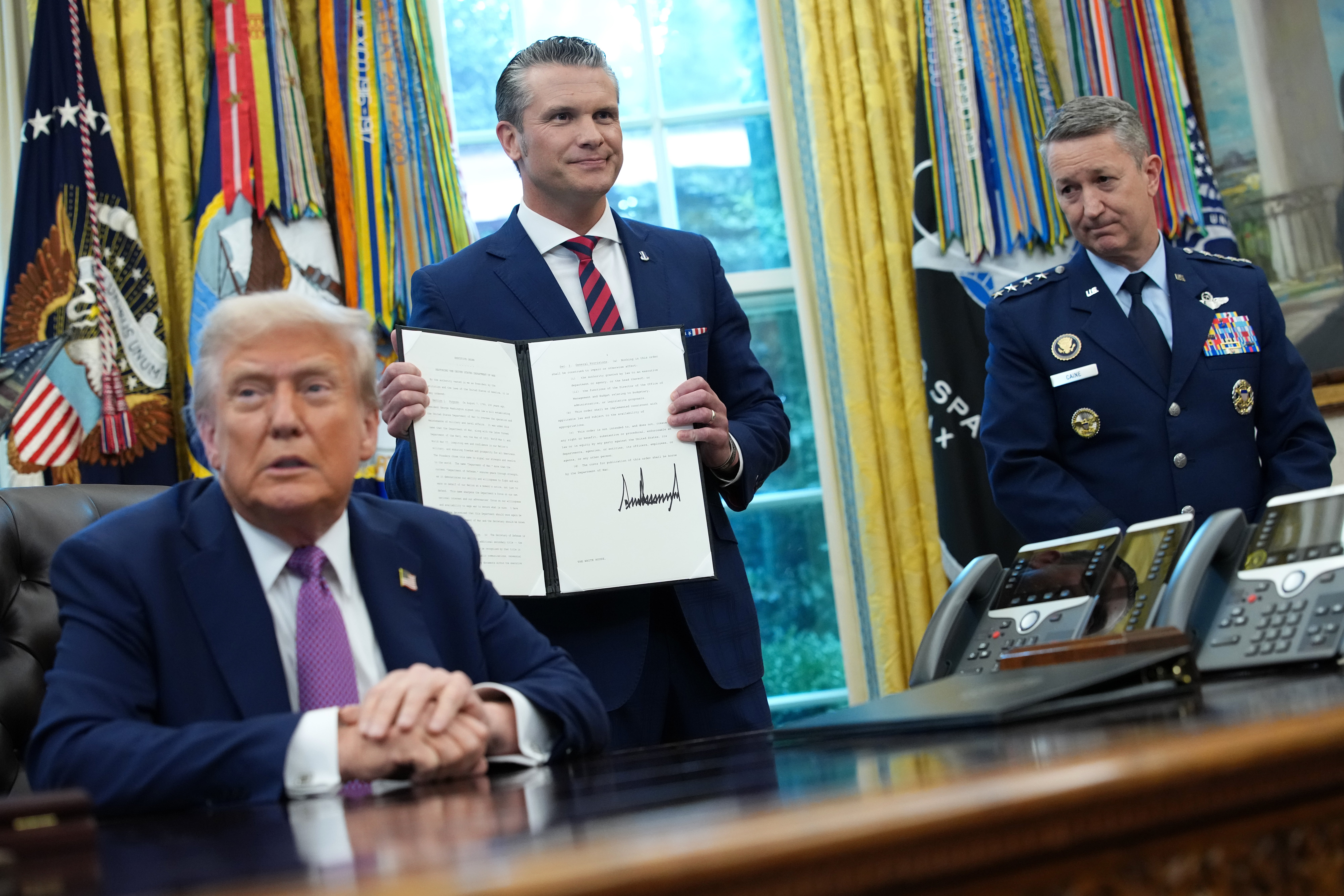 U.S. Defense Secretary Pete Hegseth (C) displays a signed executive order renaming the Department of Defense as the Department of War