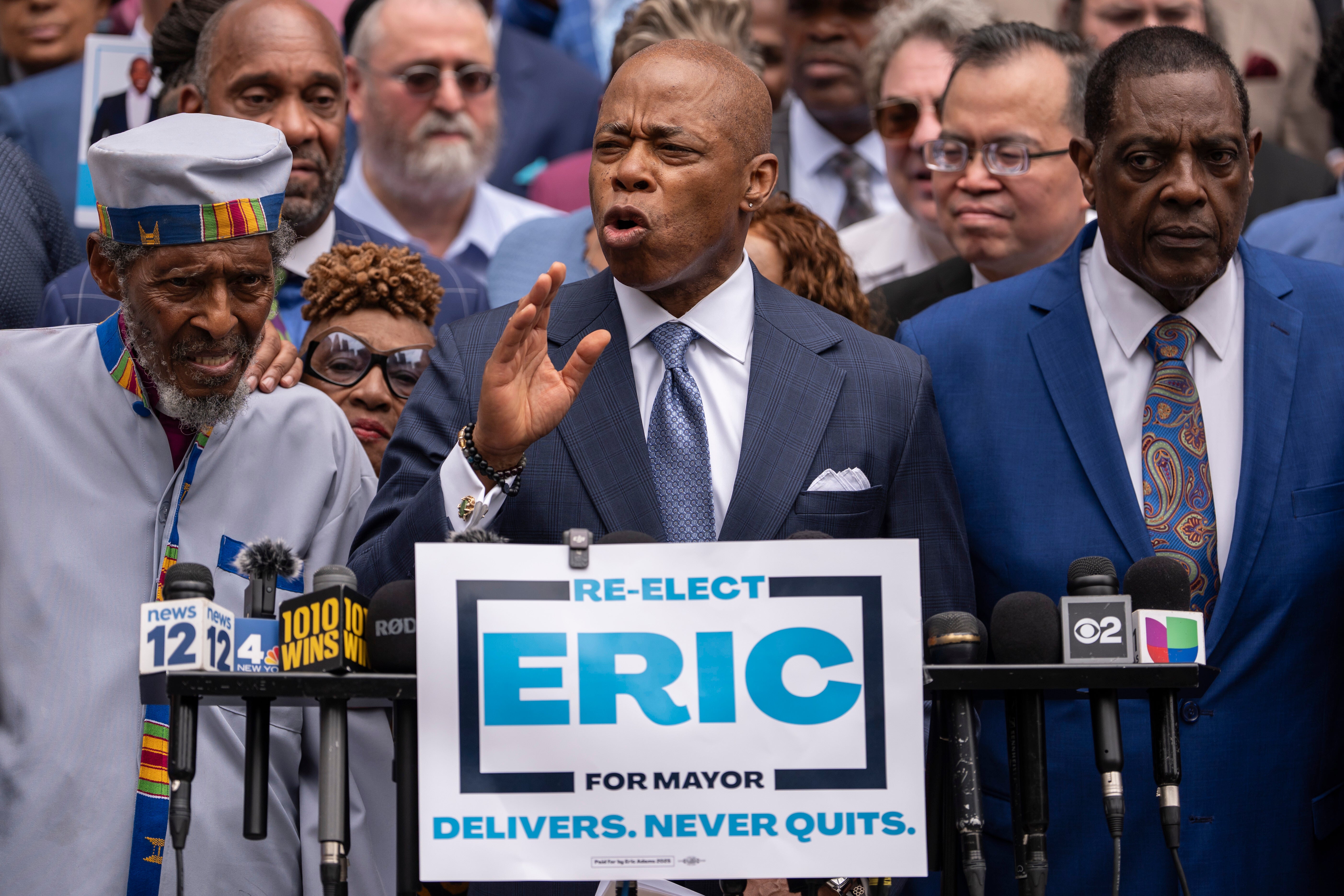 Adams pictured speaking at an event in June 2025 with a slogan that says: ‘Never quits’