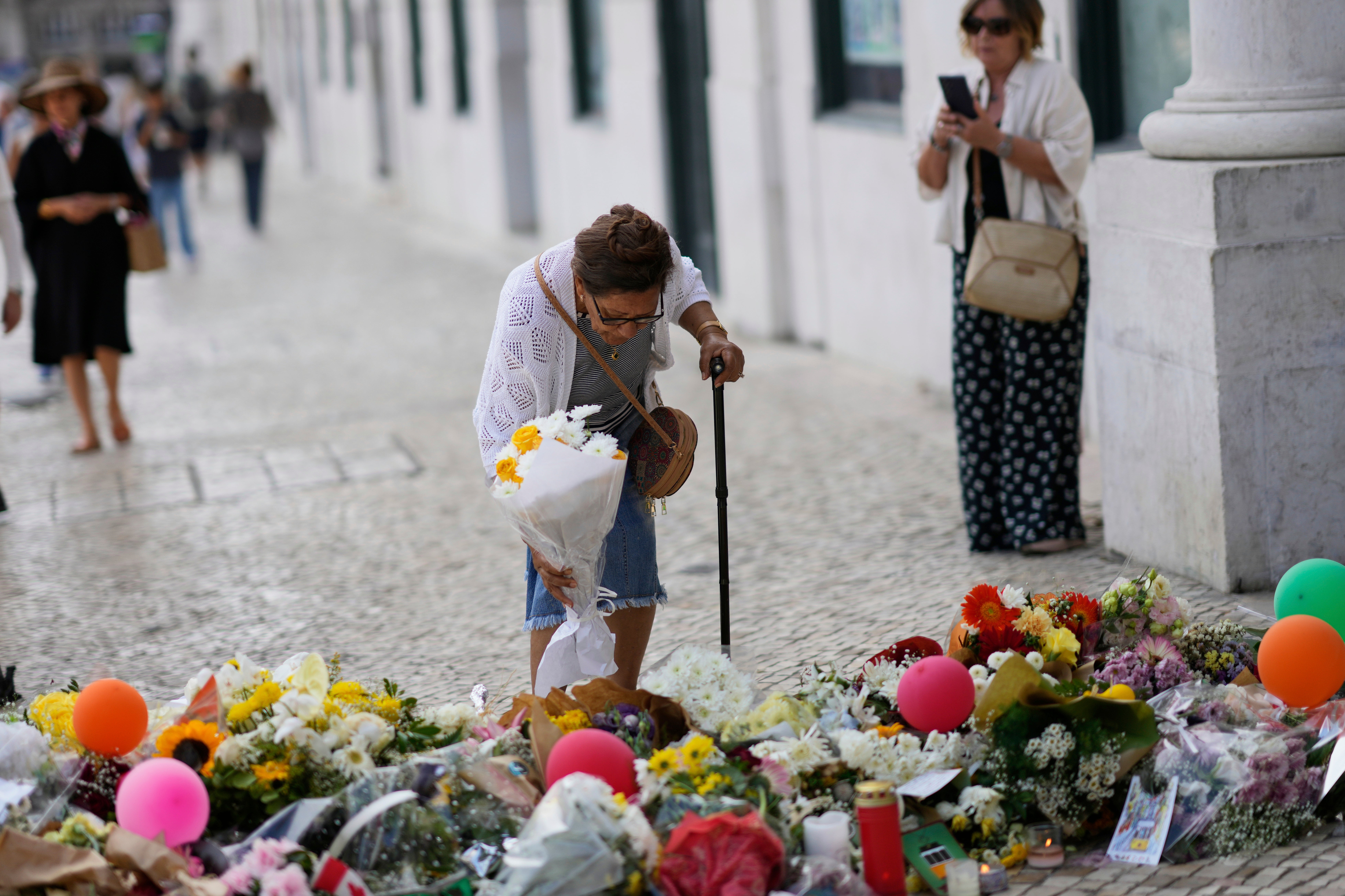An elderly woman places a bouquet of flowers at a tribute to those that perished in the Gloria funicular, a tourist streetcar that derailed and crashed, in Lisbon, Saturday, Sept. 6, 2025. (AP Photo/Armando Franca)