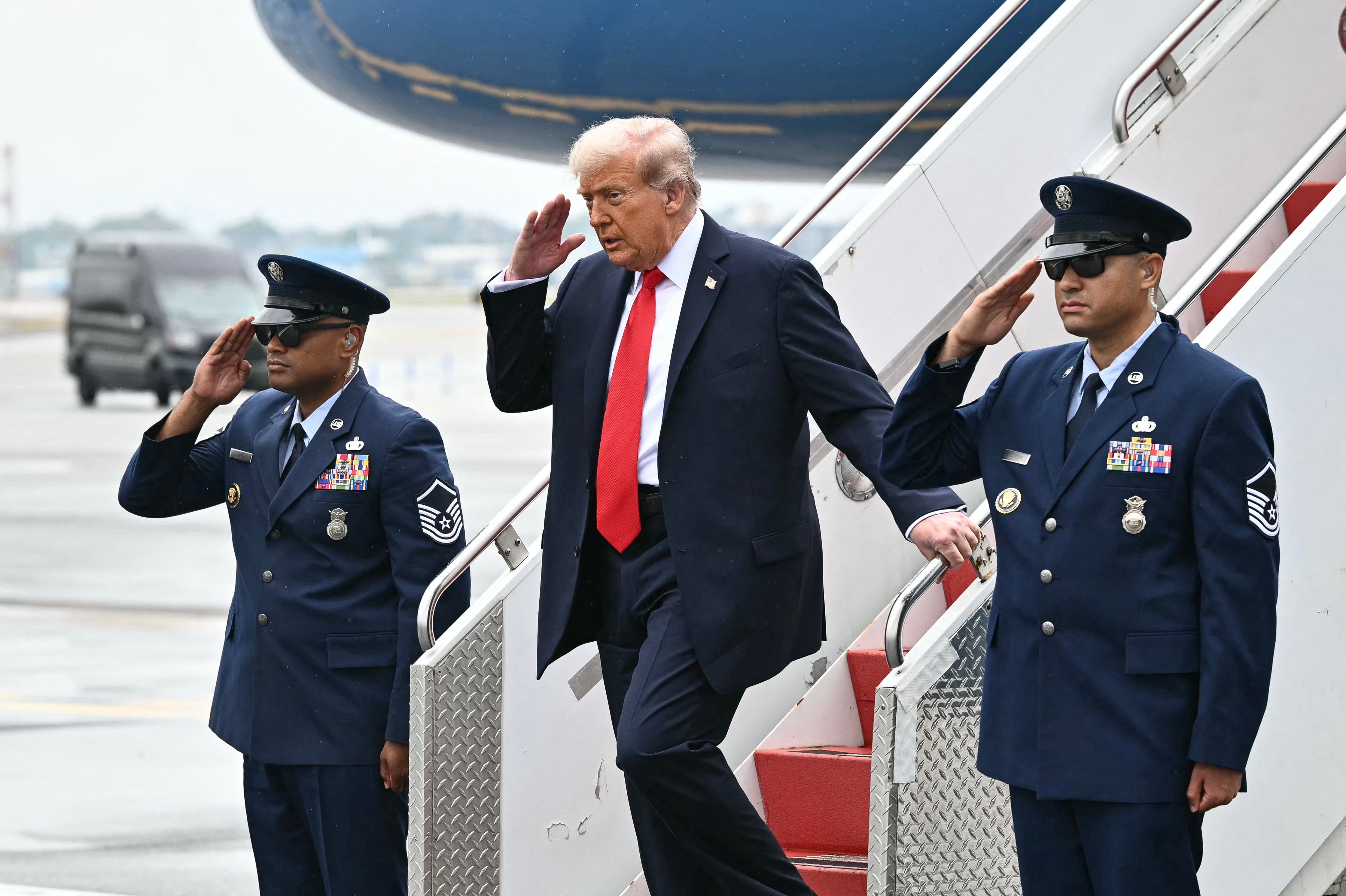 US President Donald Trump salutes as he steps off Air Force One upon arrival at LaGuardia Airport