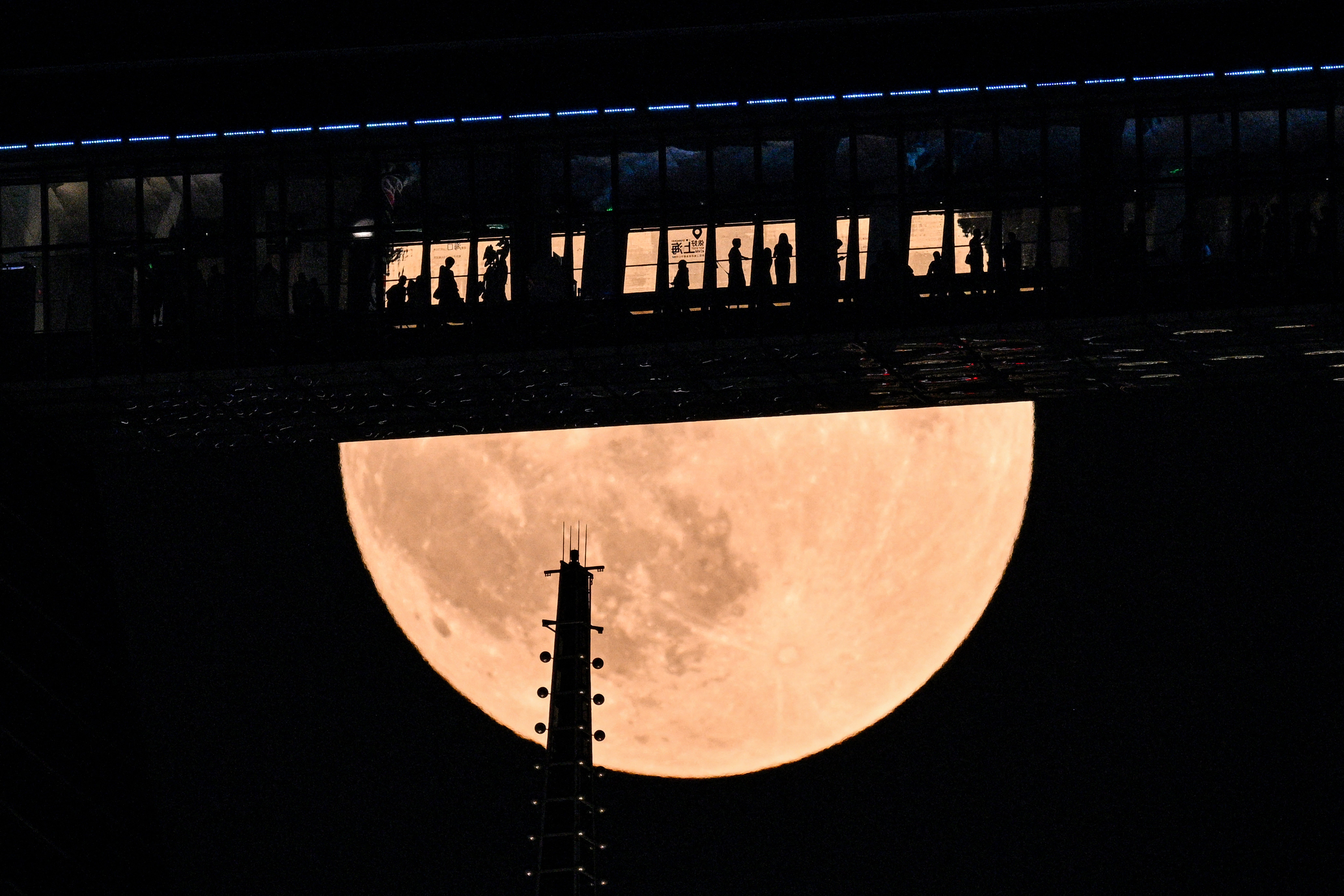 People are seen on a floor of the Shanghai World Financial Centre as a full moon, also known as the "Blood Moon," rises above skyscrapers