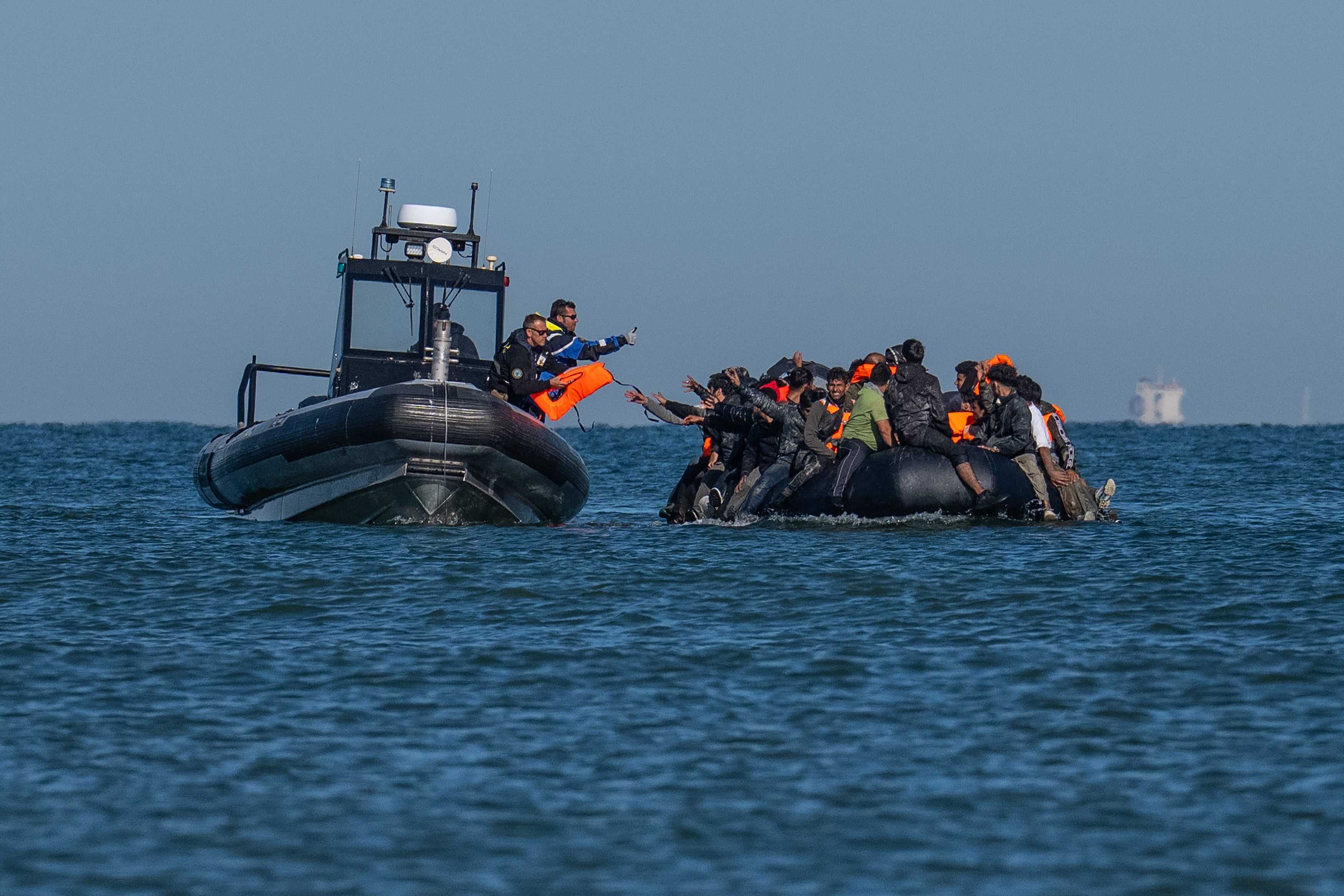 A French police vessel passes lifejackets to migrants on a dinghy as they cross the English Channel