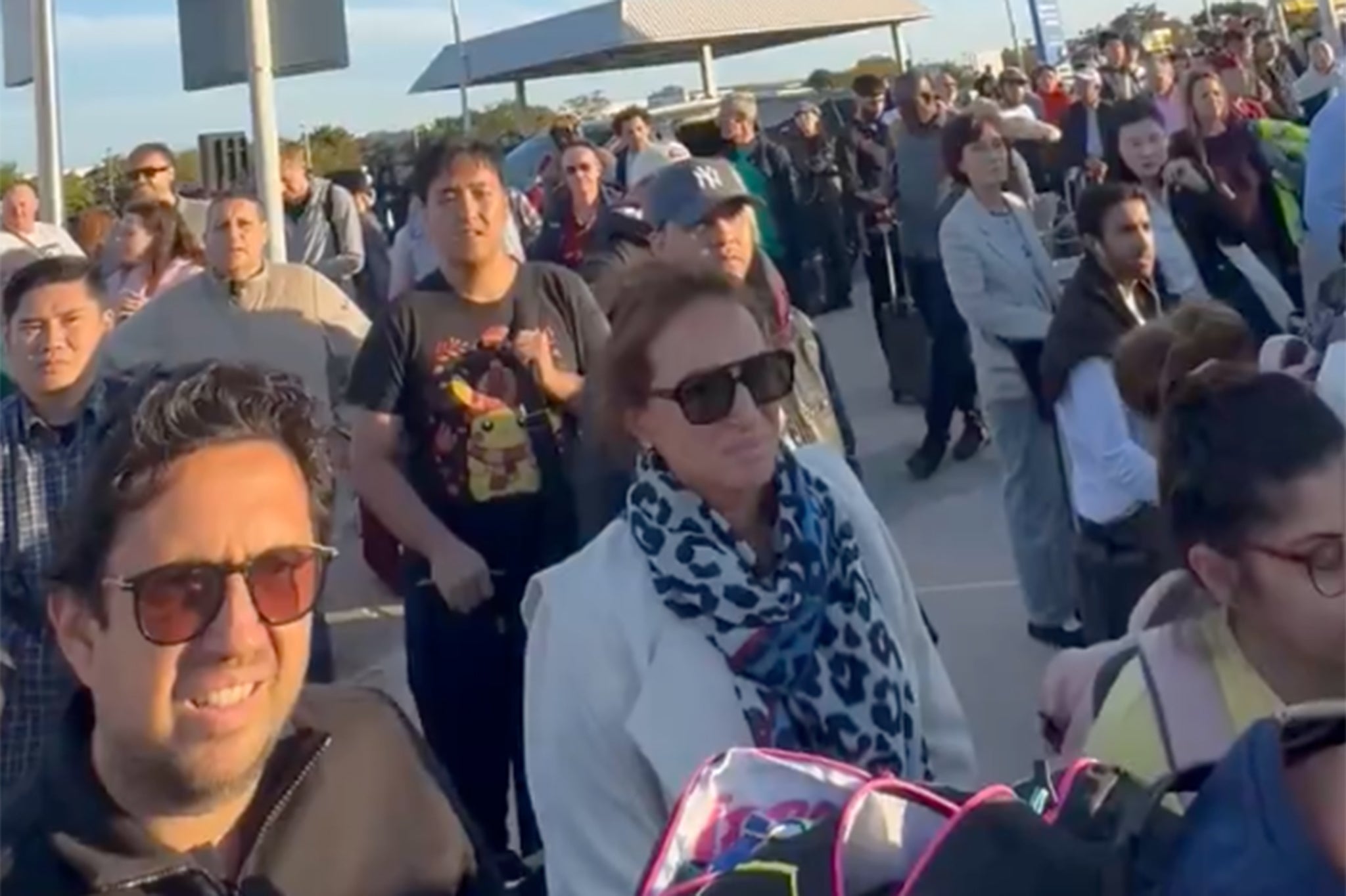 Terminal 4 travellers stand outside the airport following the evacuation