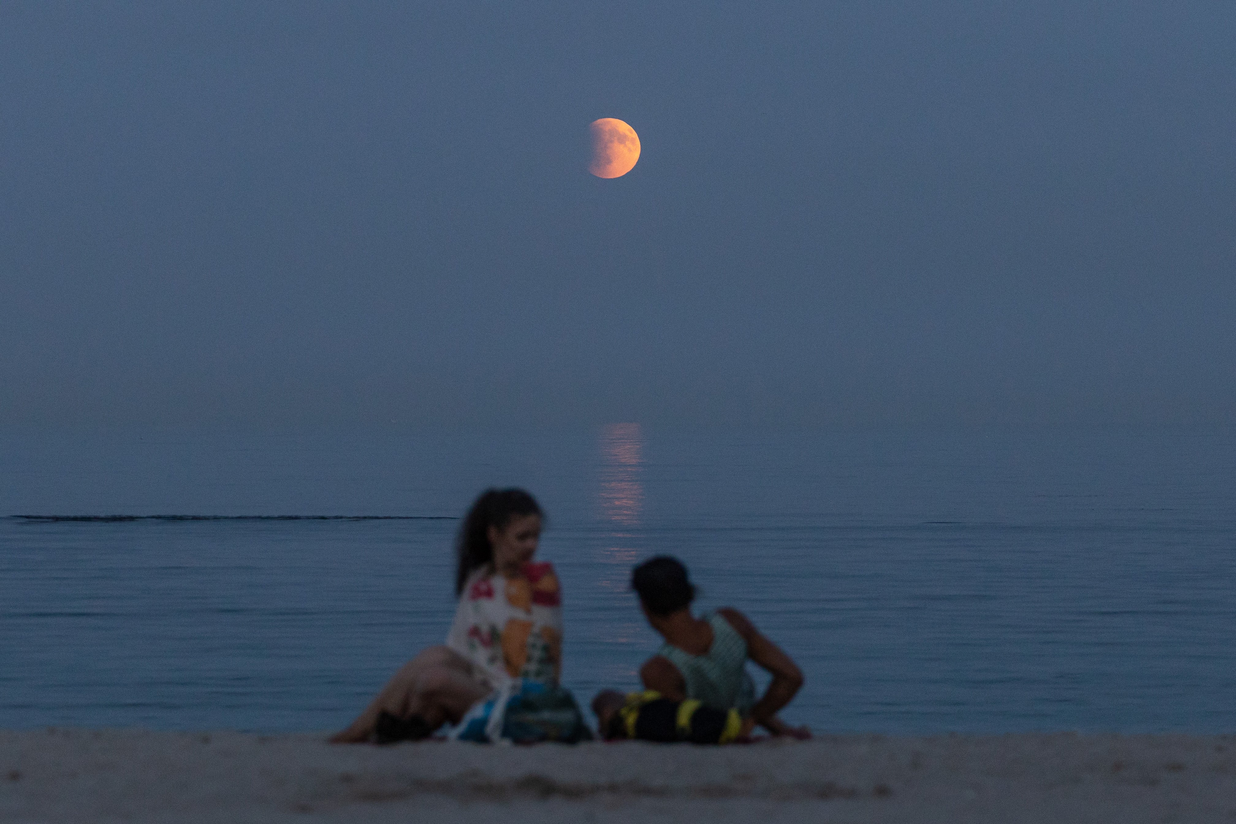 Beach-goers rest on a shore of the Black Sea with a full moon also known as "Blood Moon" during a phase of a total eclipse in the background in Odesa, on 7 September 2025