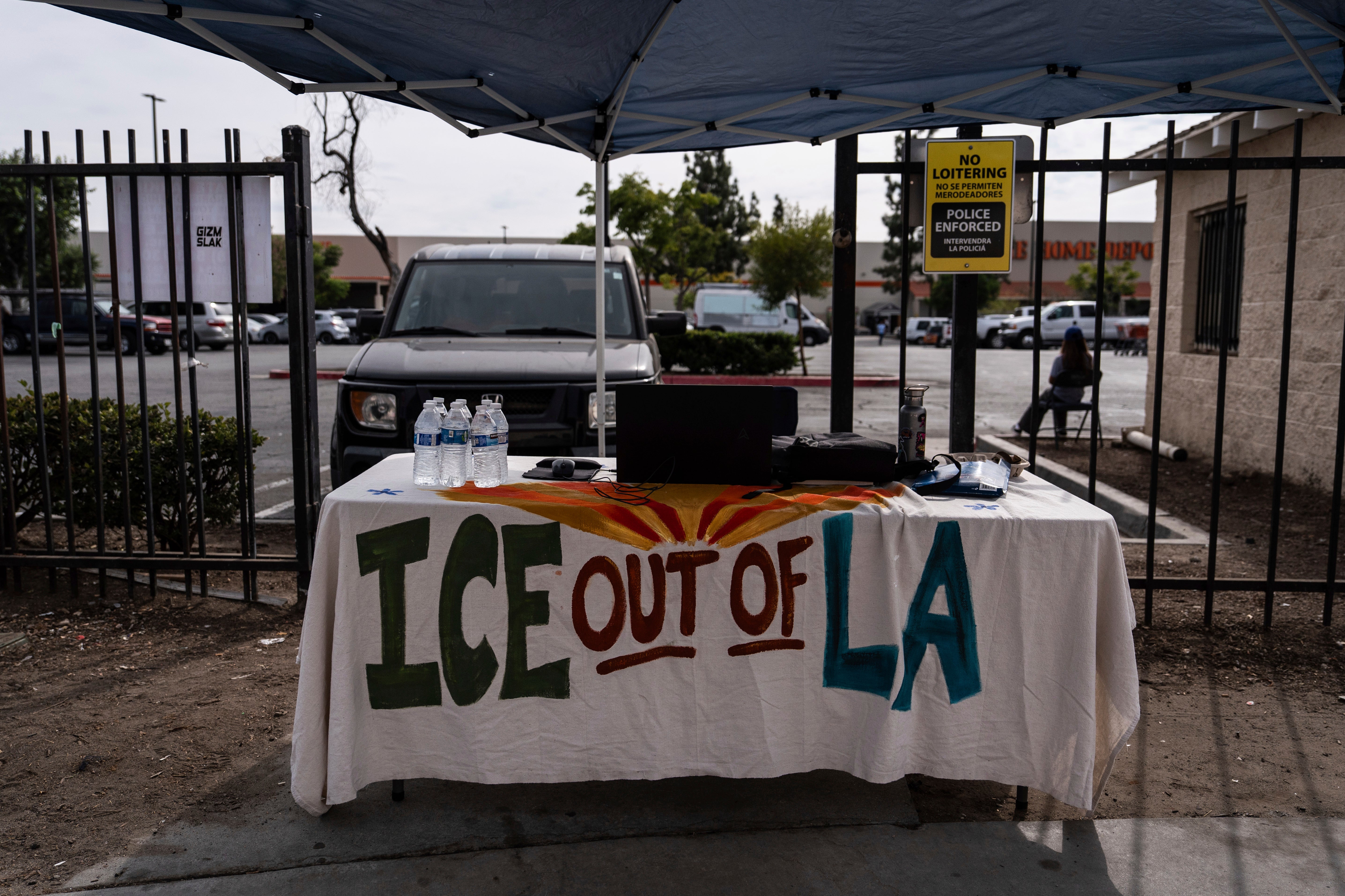A table covered with a cloth reading "ICE Out of LA" sits under a canopy next to the job center for day laborers outside a Home Depot in the Van Nuys section of Los Angeles
