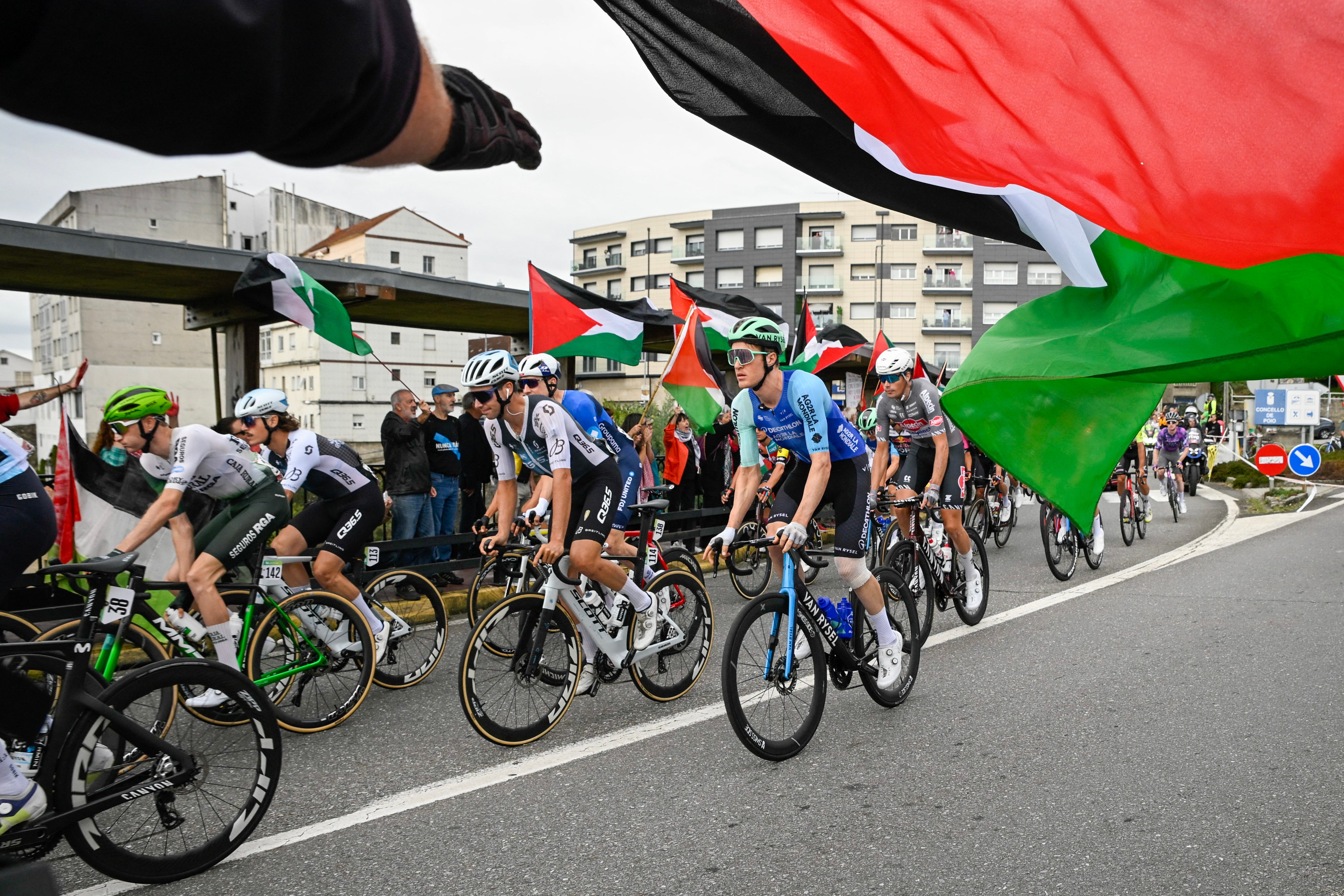Protesters wave Palestinian flags at the start line of stage 16 in Poio