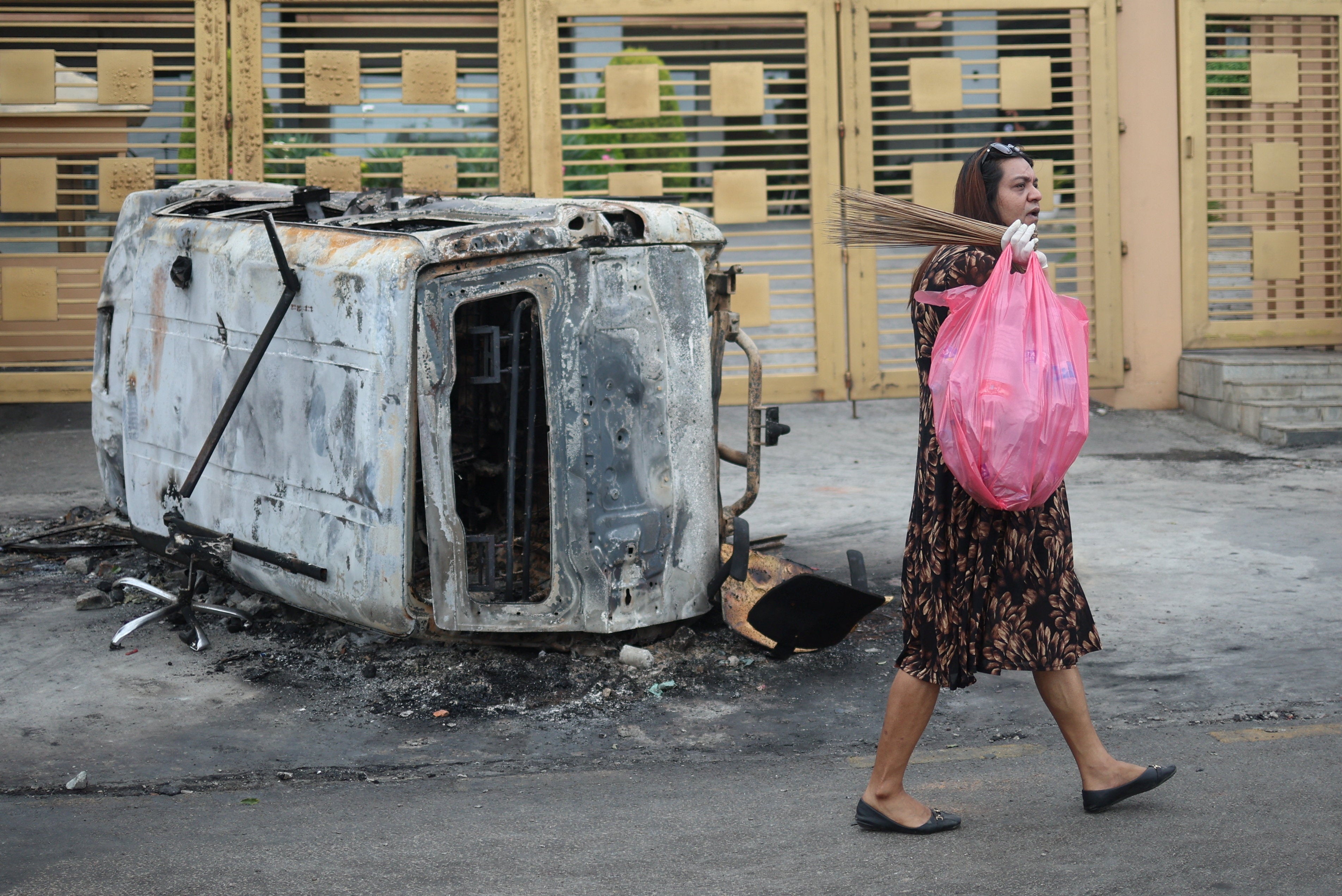 A woman walks with a garbage bag past a burnt vehicle in Kathmandu