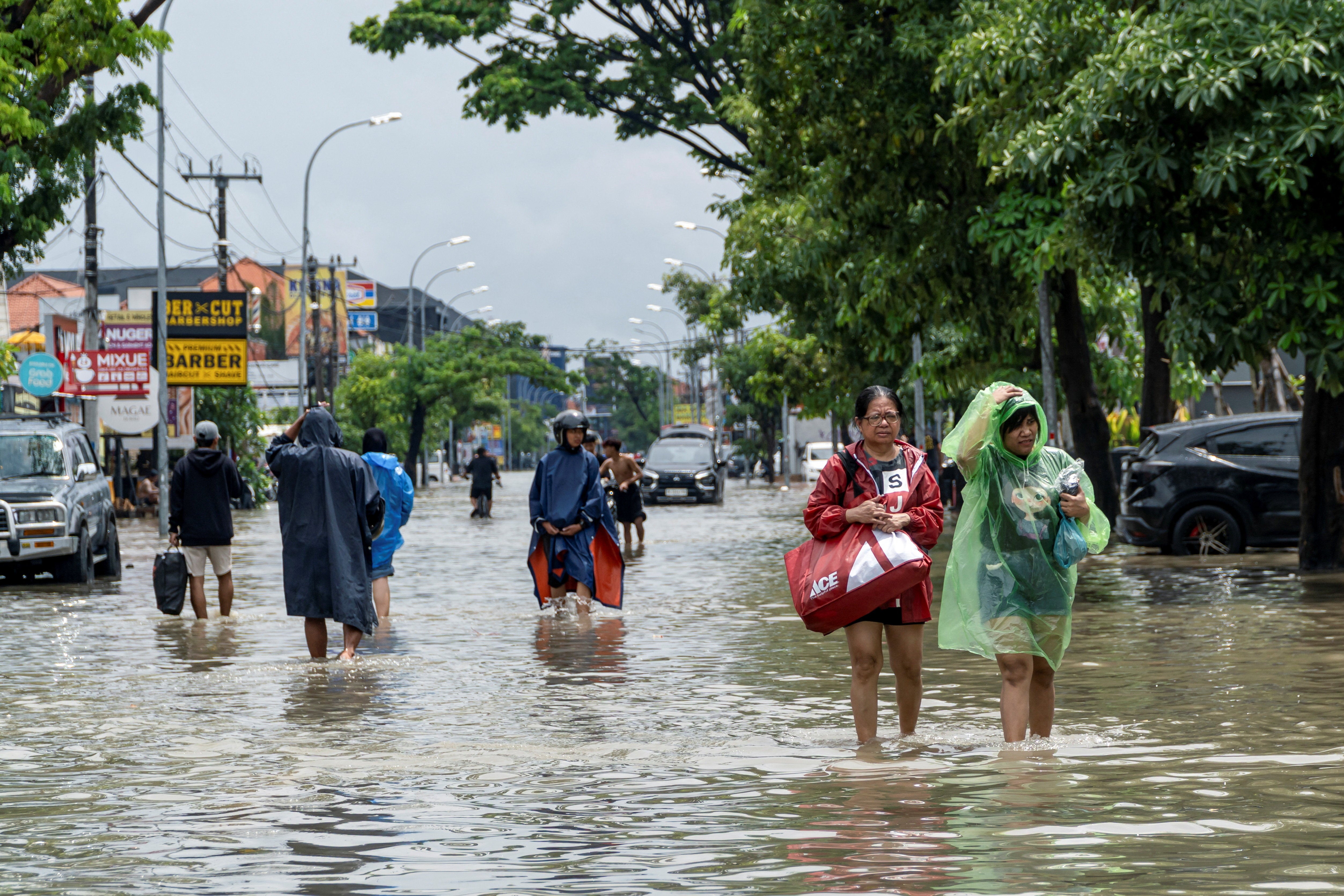 People wade through a flooded street following overnight heavy rains in Legian, Badung, Bali