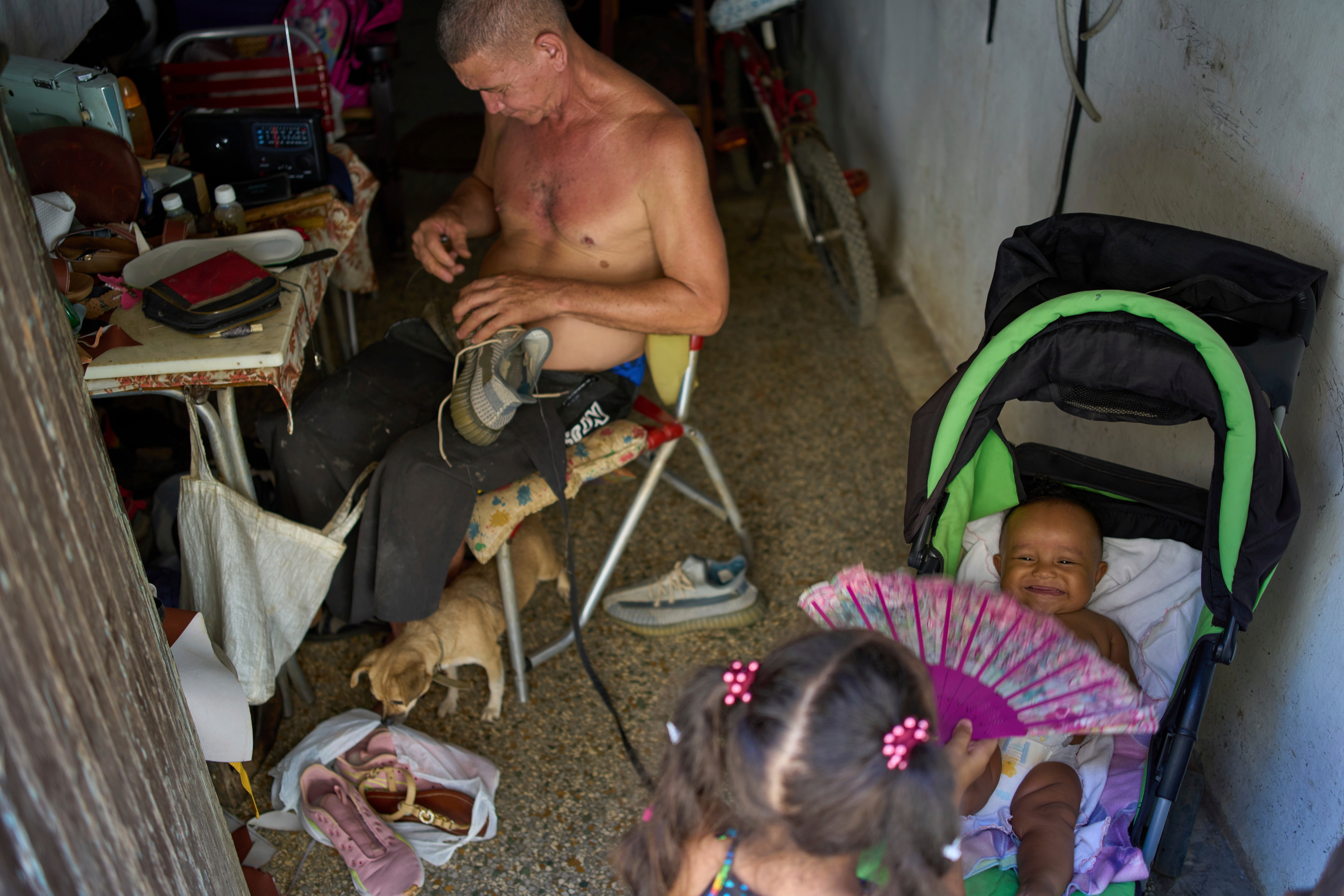 A girl cools a baby off with a fan as a man repairs shoes during a blackout in Havana