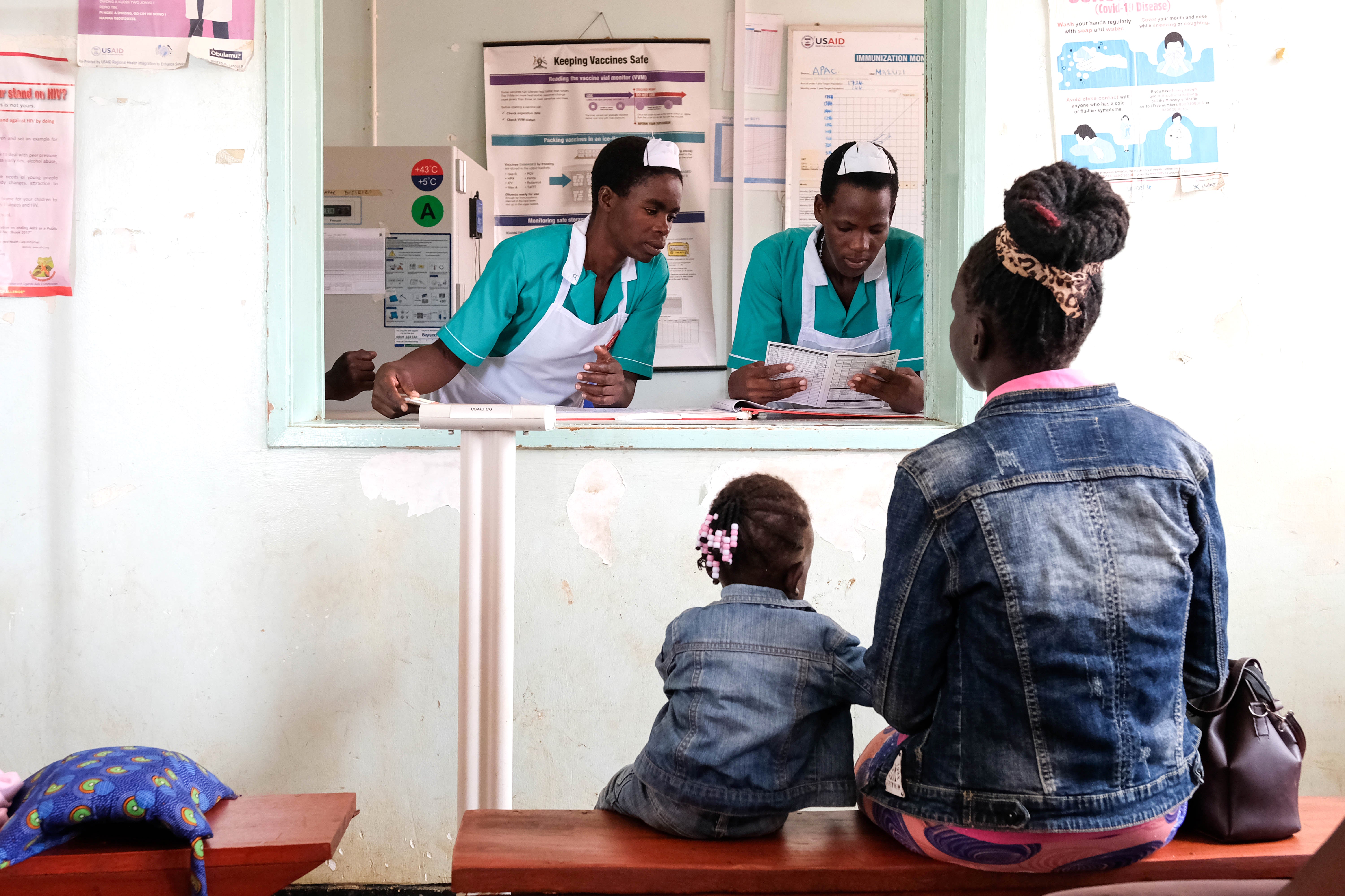 A mother and child wait as medical interns register details of the child before receiving a malaria vaccine in Uganda