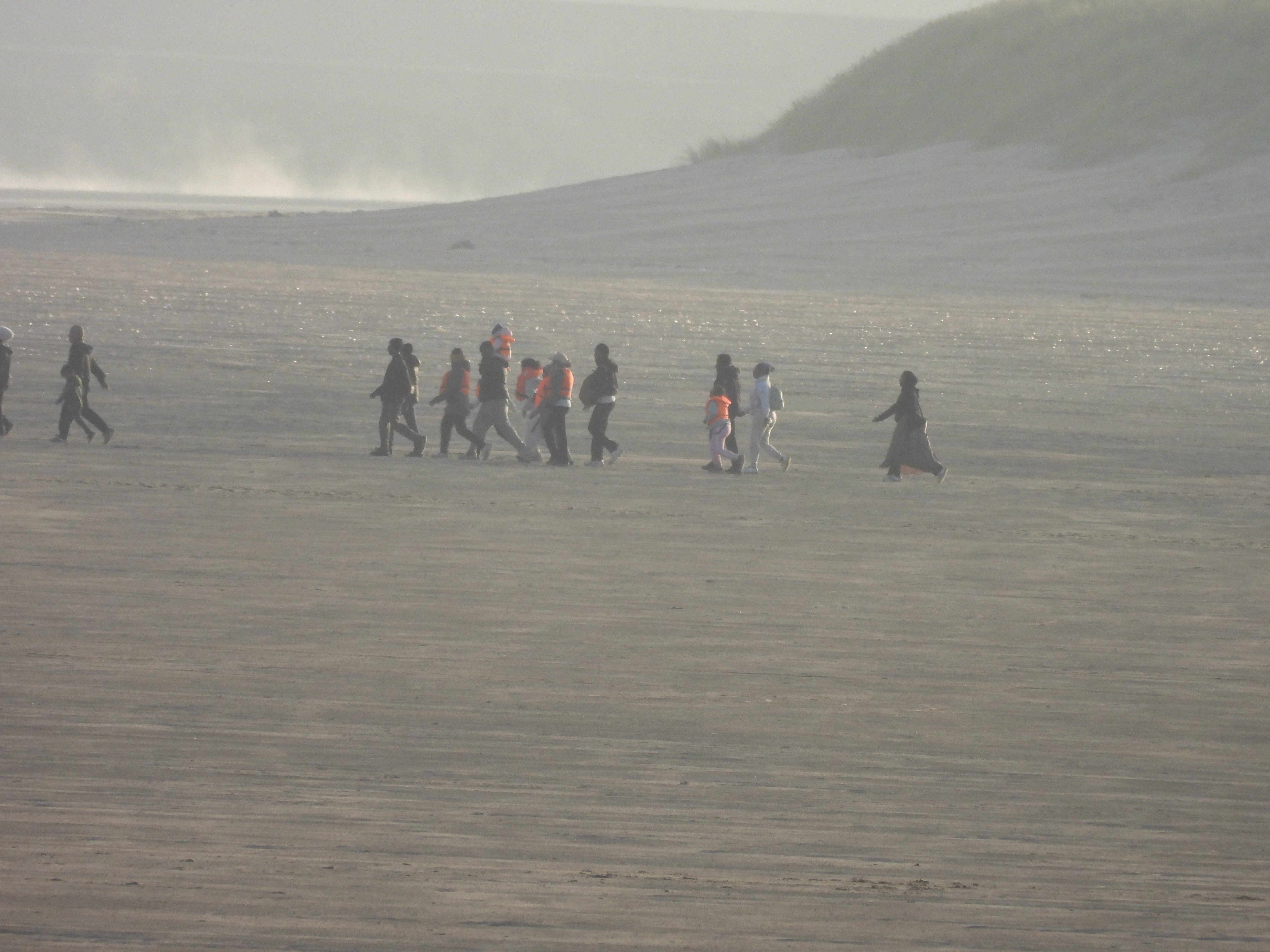 A group of migrants, including women and children, heads across the beach to a boat waiting in the shallows