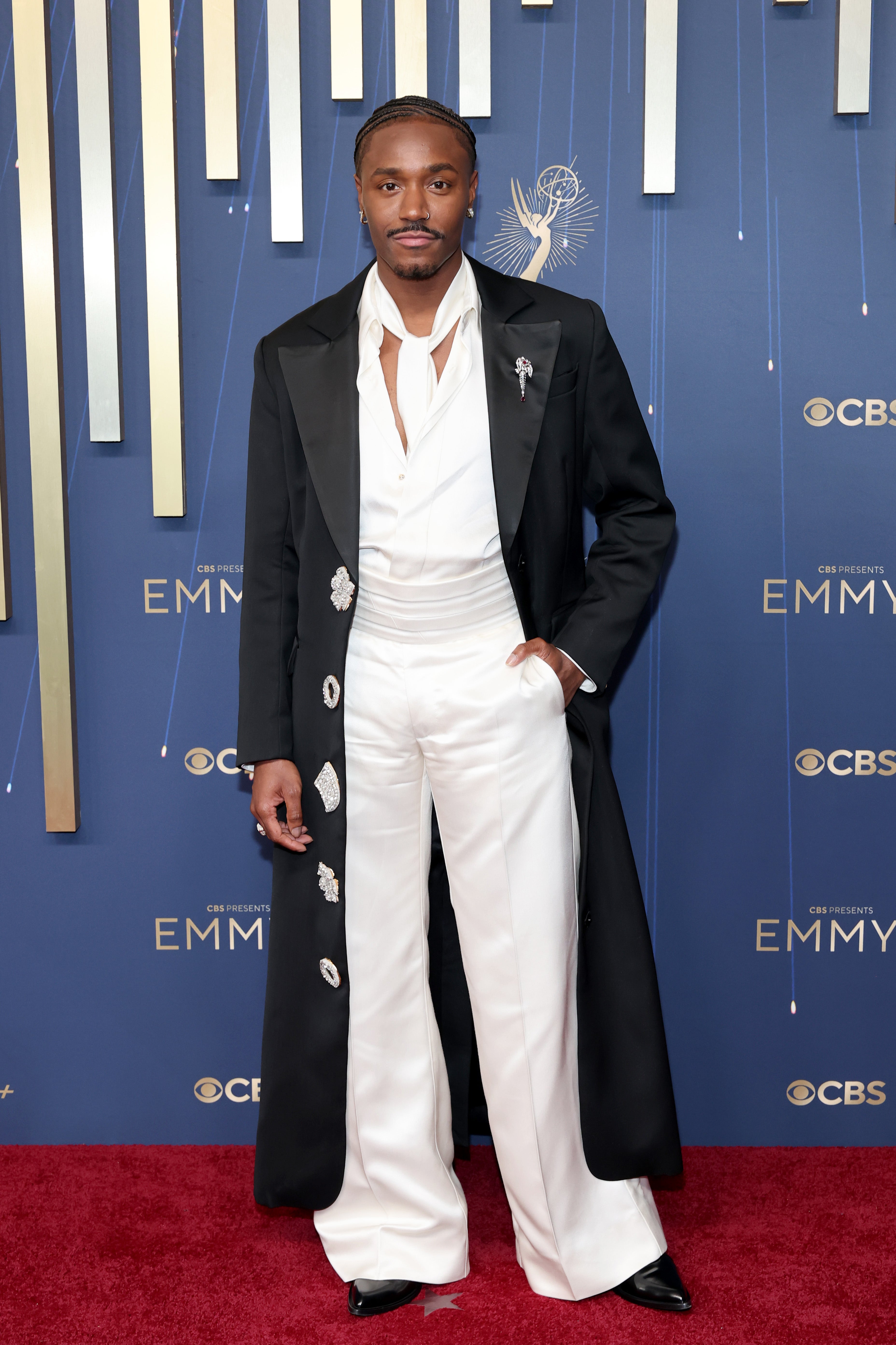Dewayne Perkins posed in a well-tailored white pantsuit and a black floor-length jacket, seemingly inspired by this year’s Met Gala theme: Black Dandyism. His black pointed shoes, white loose tie, and the silver pendants on his jacket made for a show-stopping look
