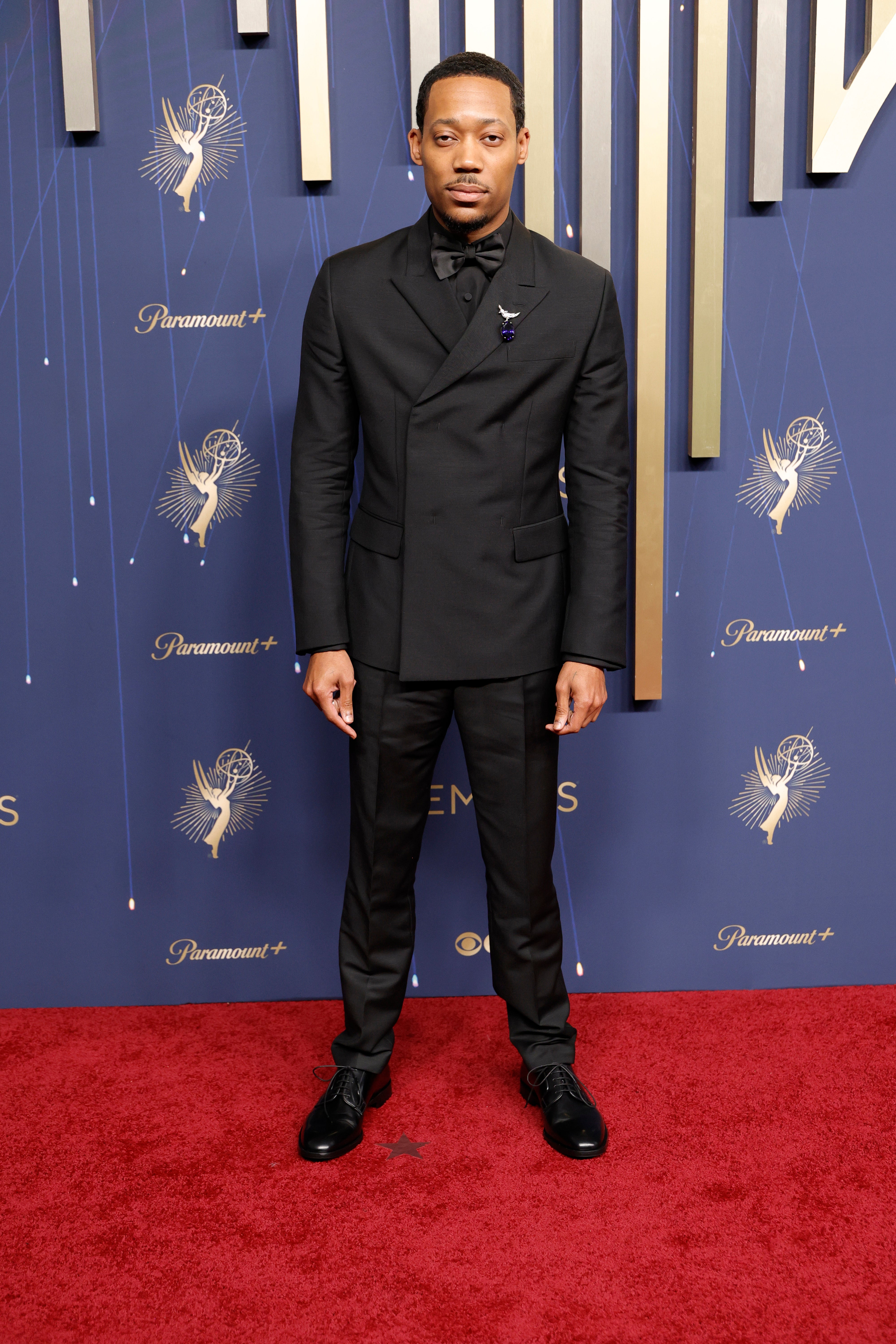 Tyler James Williams is embracing an all-black look tonight, wearing a tuxedo, matching bowtie, and leather shoes. He also had a silver brooch on his jacket