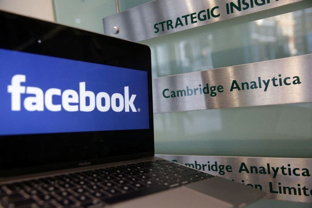 A laptop showing the Facebook logo is held alongside a Cambridge Analytica sign at the entrance to the building housing the offices of Cambridge Analytica, in central London on 21 March, 2018