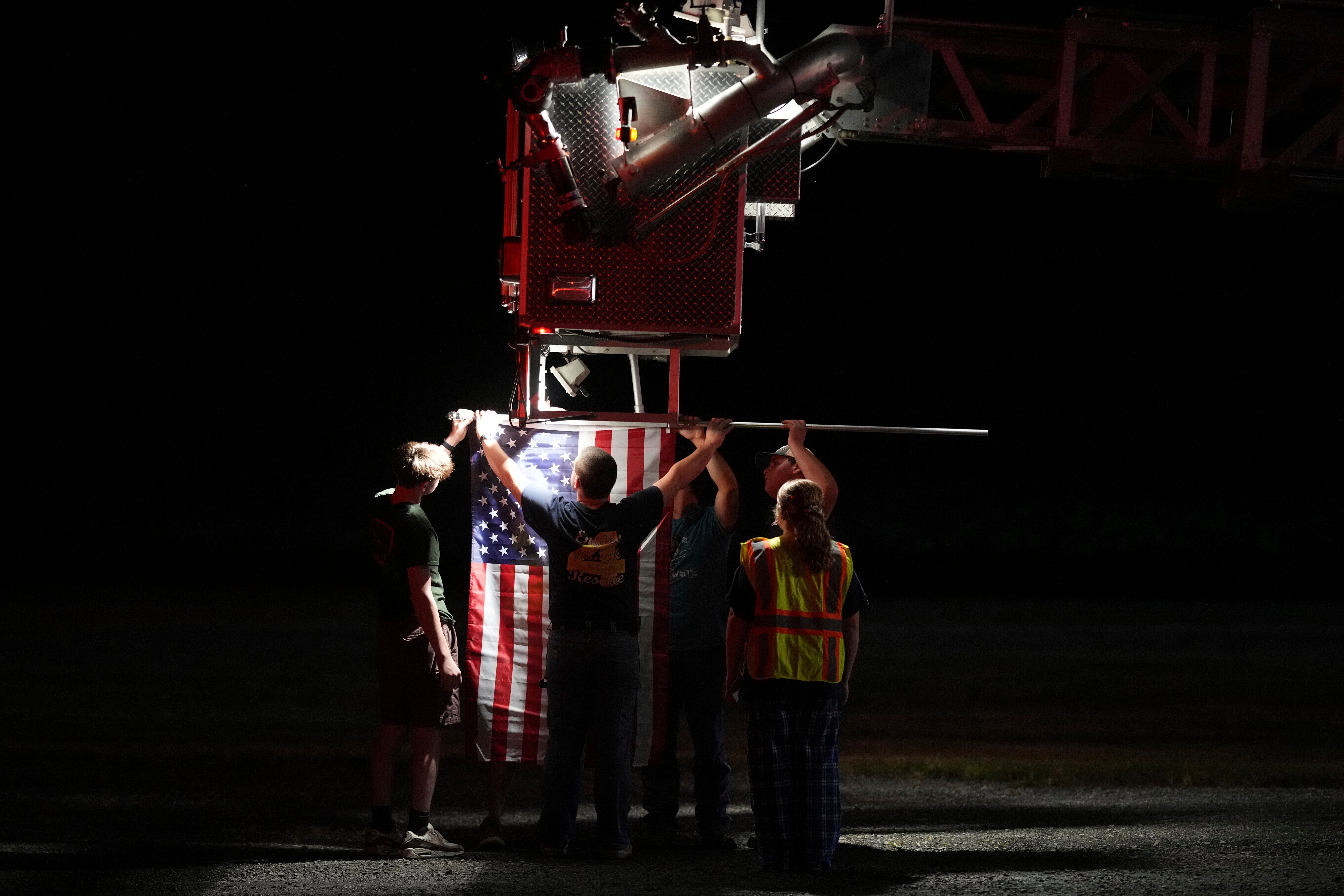 As equipes de bombeiros conectam uma bandeira americana a um Fietterk antes de uma procissão ser morta a tiros na quarta -feira depois de matar vários policiais