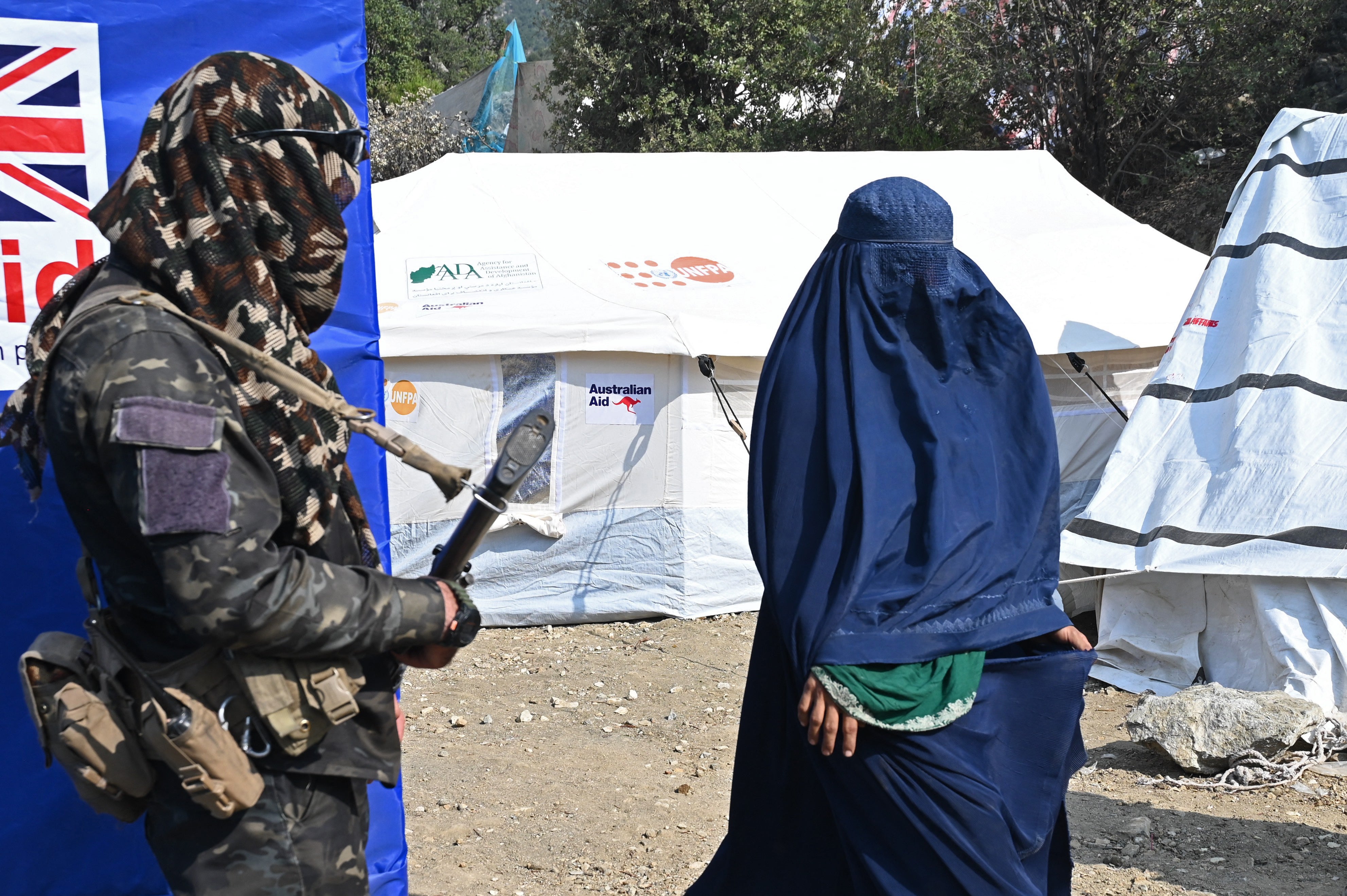 An Afghan security personnel stands guard as a woman walks past a mobile health clinic in Kunar
