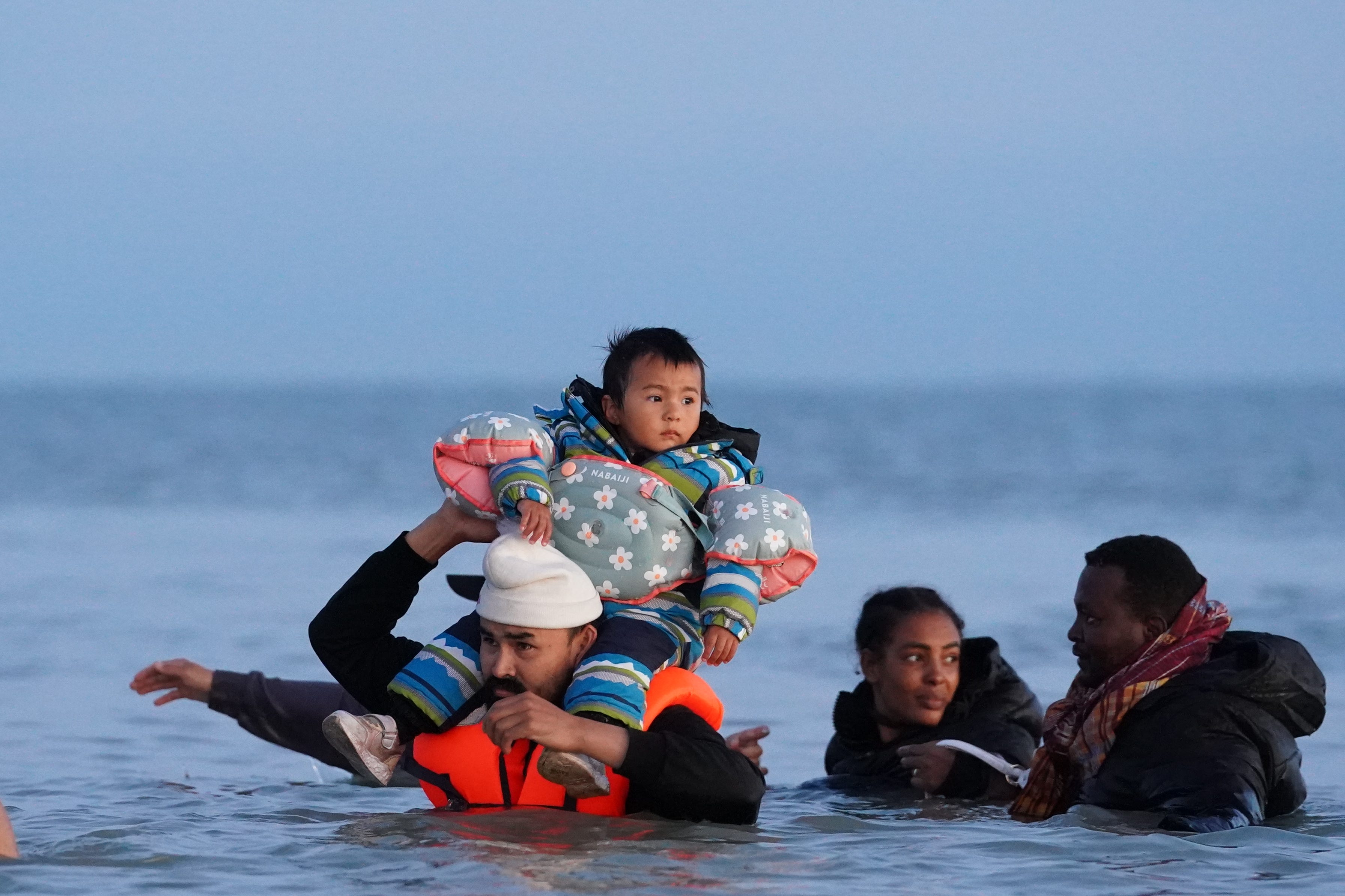 A group of people, including a child on a man’s shoulders, thought to be migrants wade into the sea near Gravelines in France (Gareth Fuller/PA)