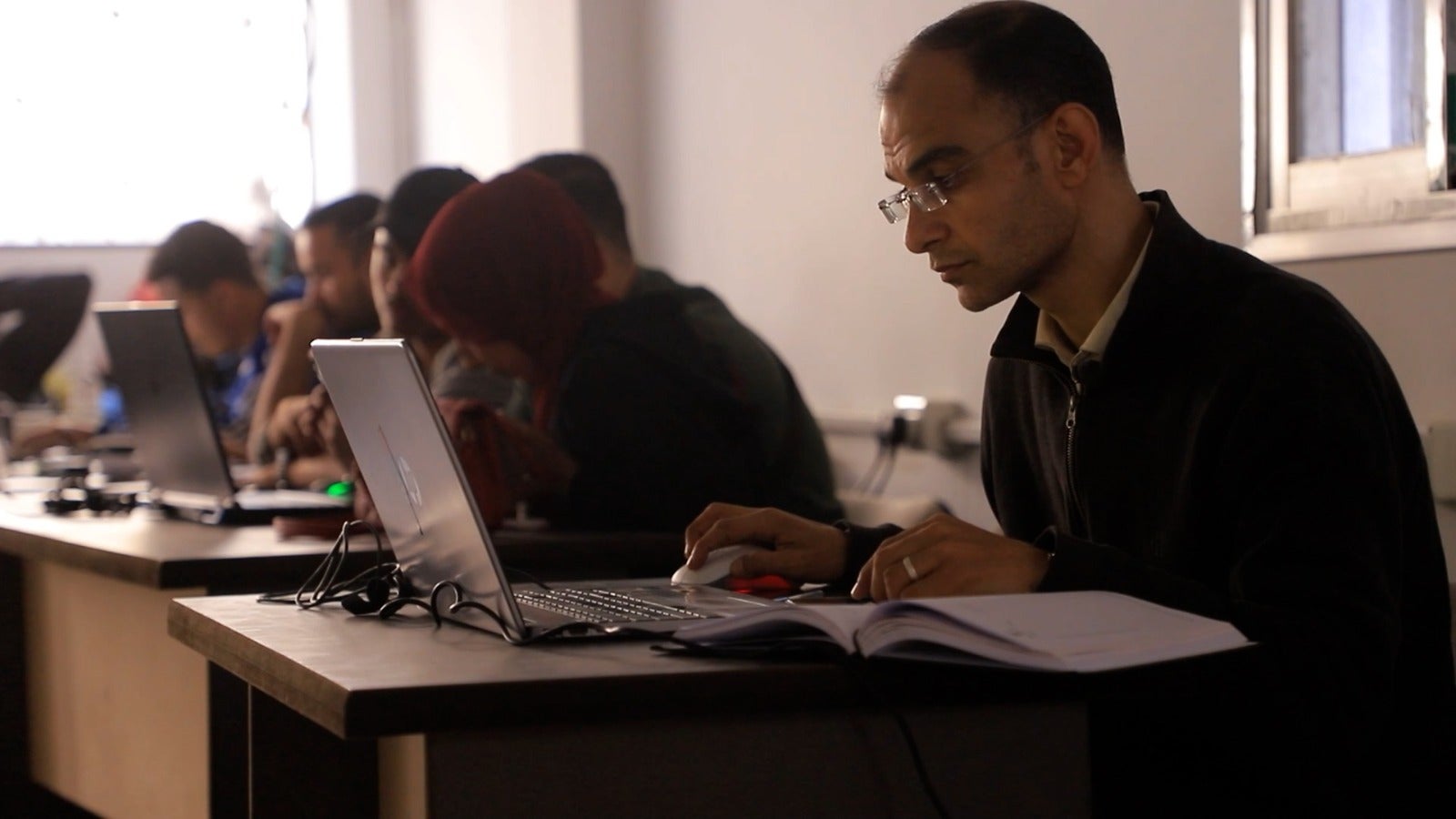 The author working in an internet cafe: ‘Students reach out whenever the internet briefly holds. I receive WhatsApp messages, hurried voice notes, and photos of handwritten assignments captured in fleeting moments of connectivity’